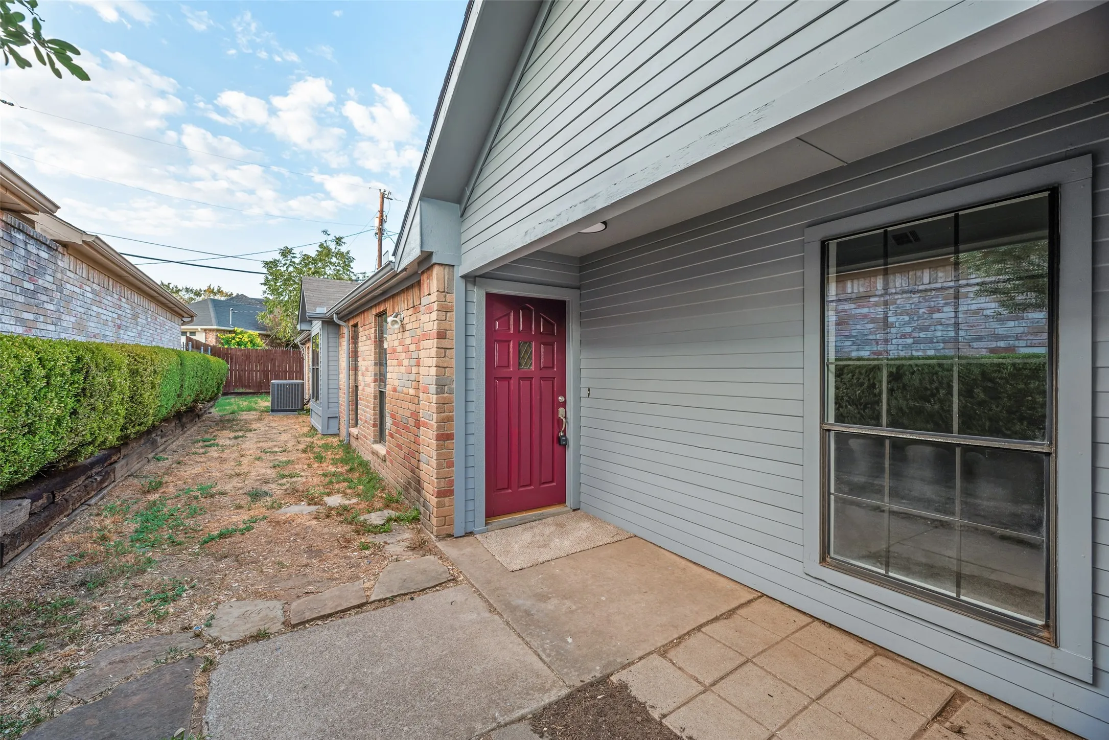 Exterior featuring brick and horizontal siding, a red entry door, a window with grid inserts, and a concrete walkway