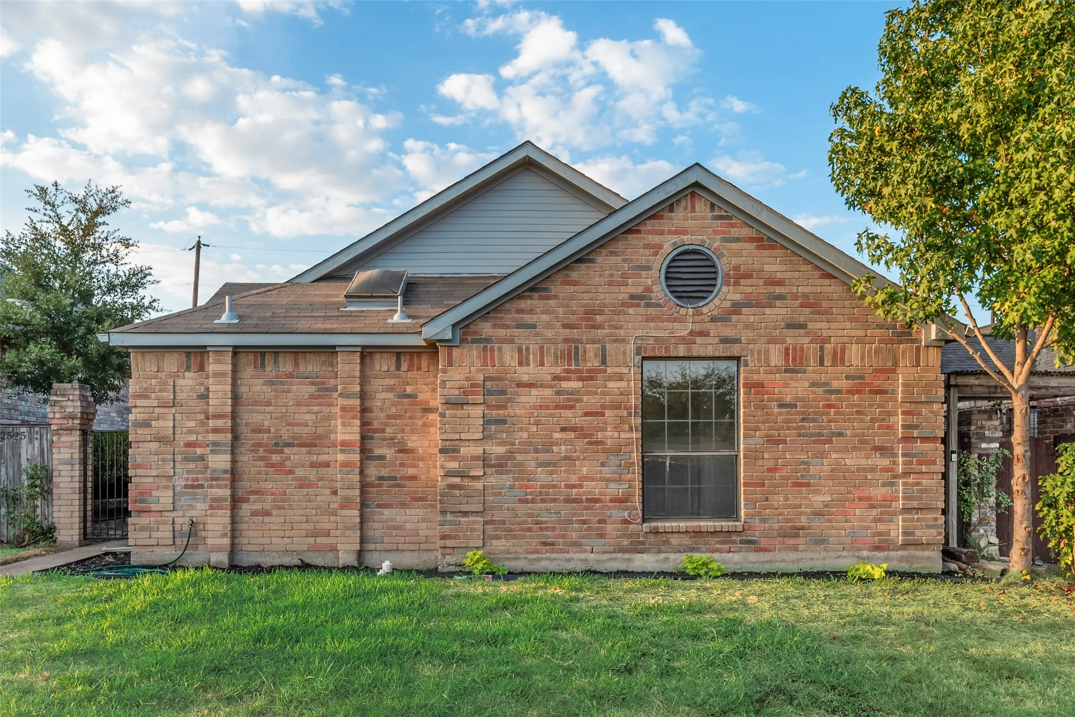 Brick exterior with a gabled roofline, round louvered vent, and established greenery