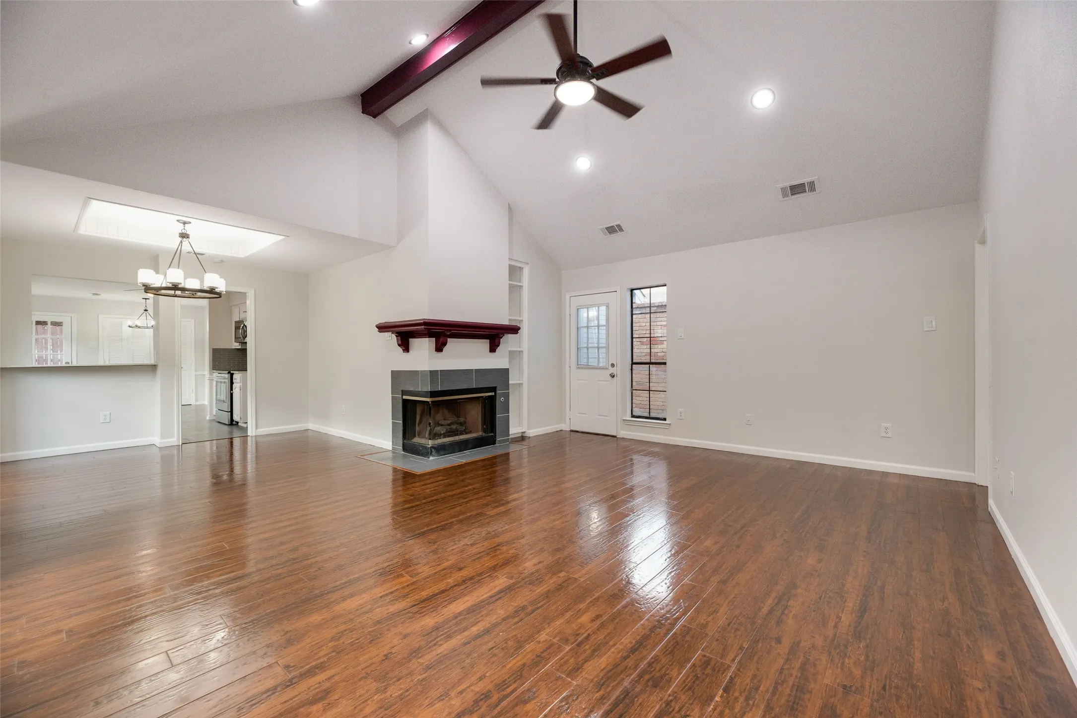 Vaulted ceiling with exposed beam, wood-finish flooring, recessed lighting, ceiling fan, and a tiled fireplace with wood mantel