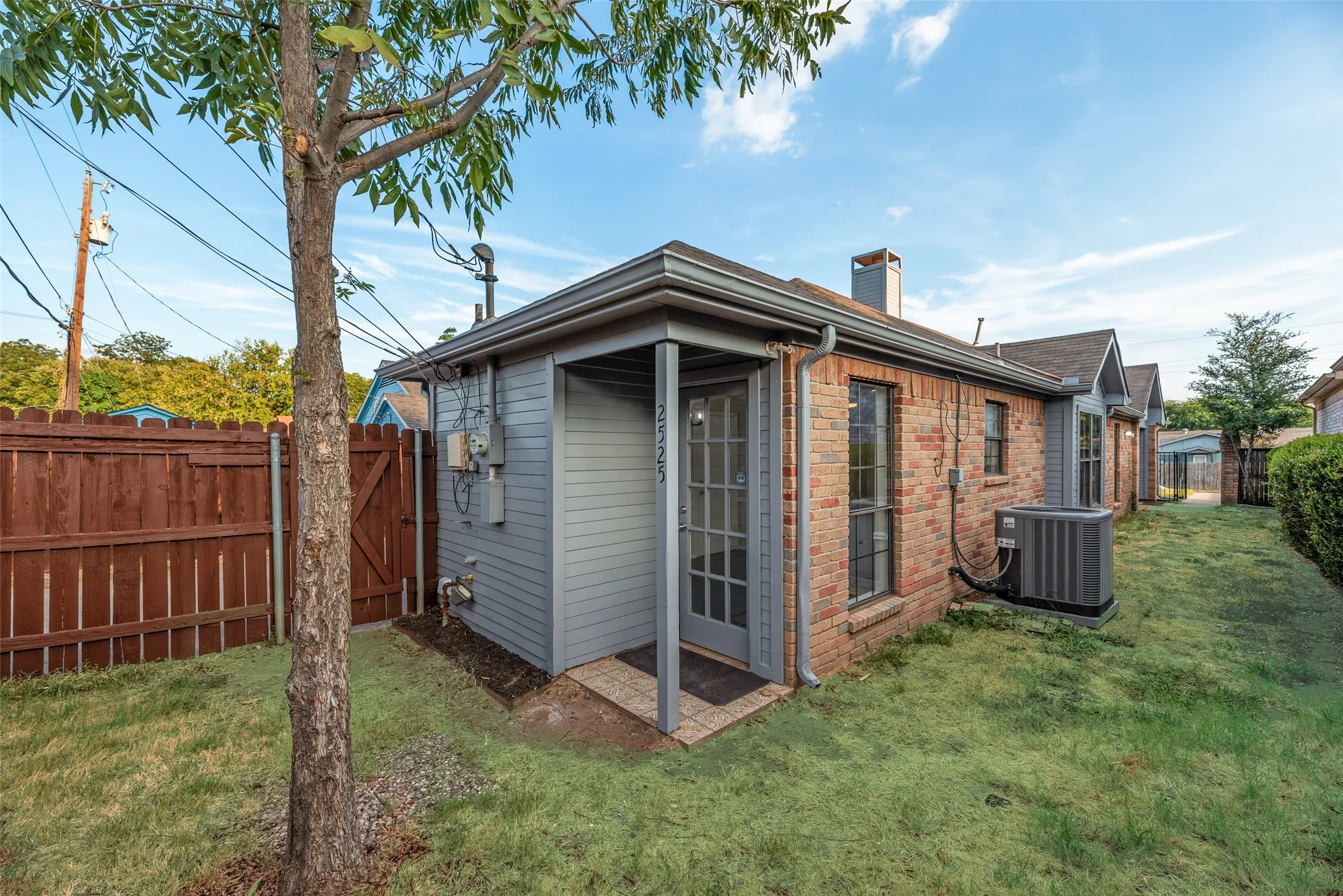 Brick exterior with a covered entry, gabled roofline, privacy fence, and manicured lawn