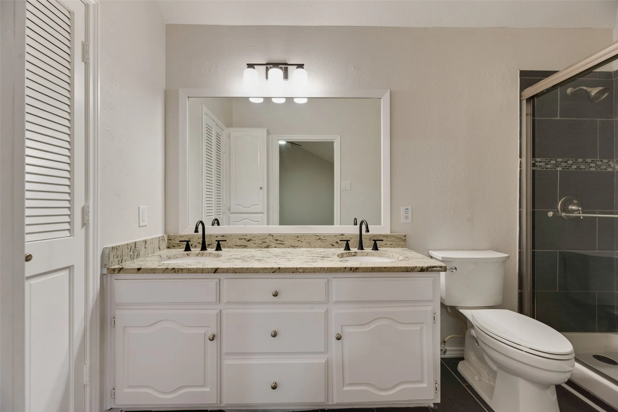 Dual vanity with granite countertop, white cabinetry, and matte black fixtures