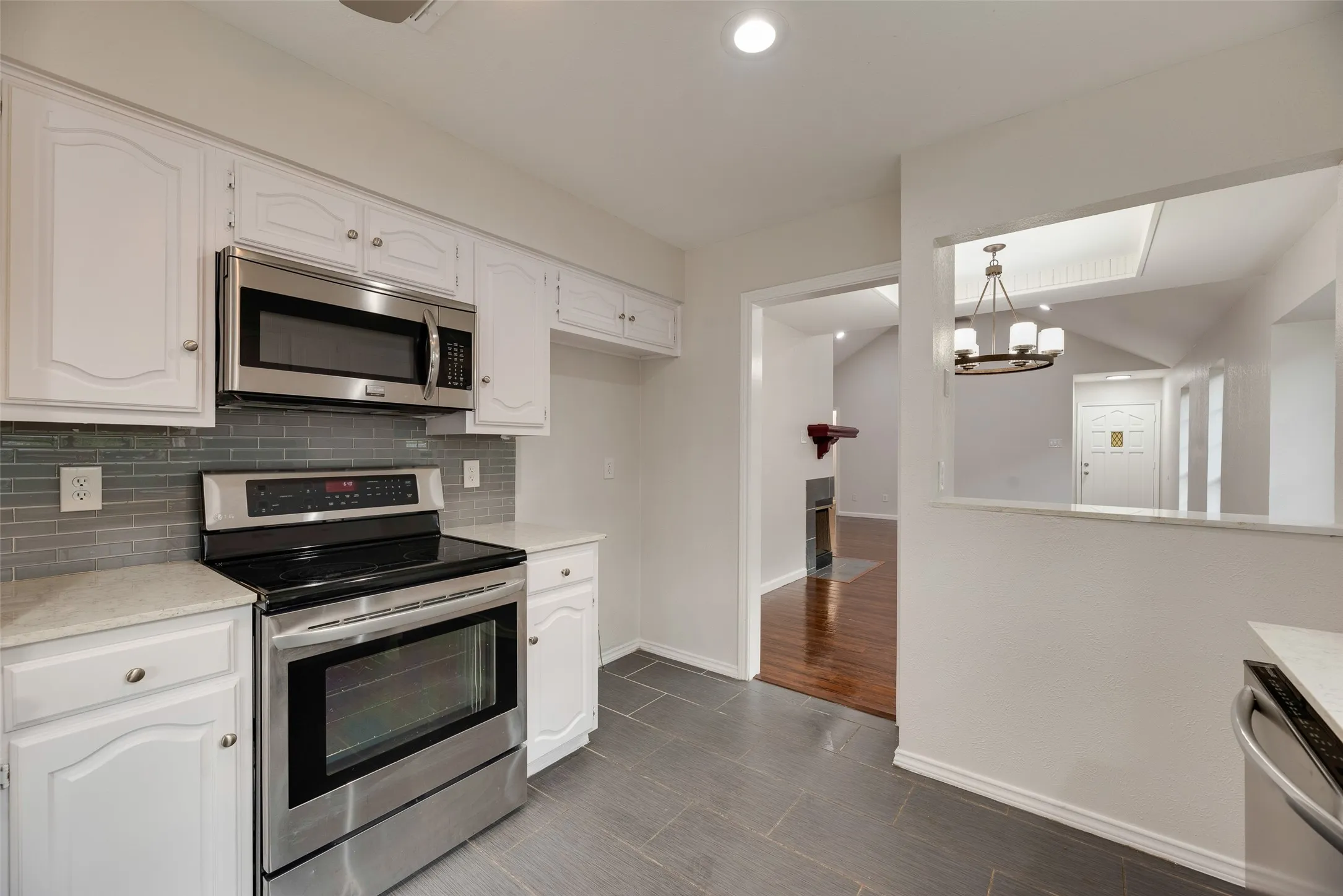Stainless steel appliance suite, white cabinetry, tile backsplash, and stone-finish countertops