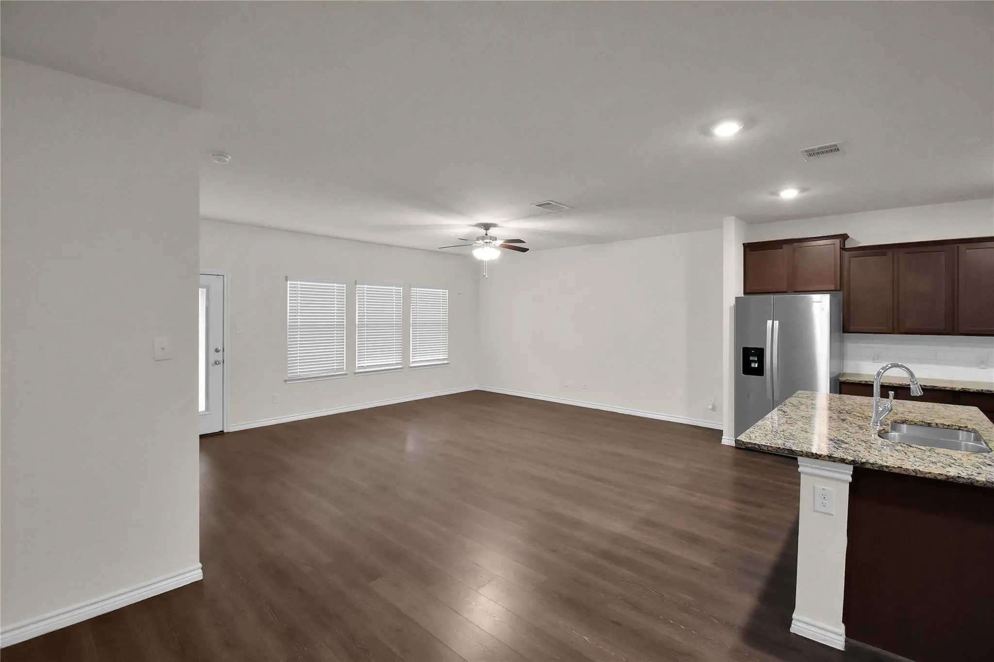 Expansive open-concept space featuring wood-finish flooring, a ceiling fan, and multiple windows with blinds