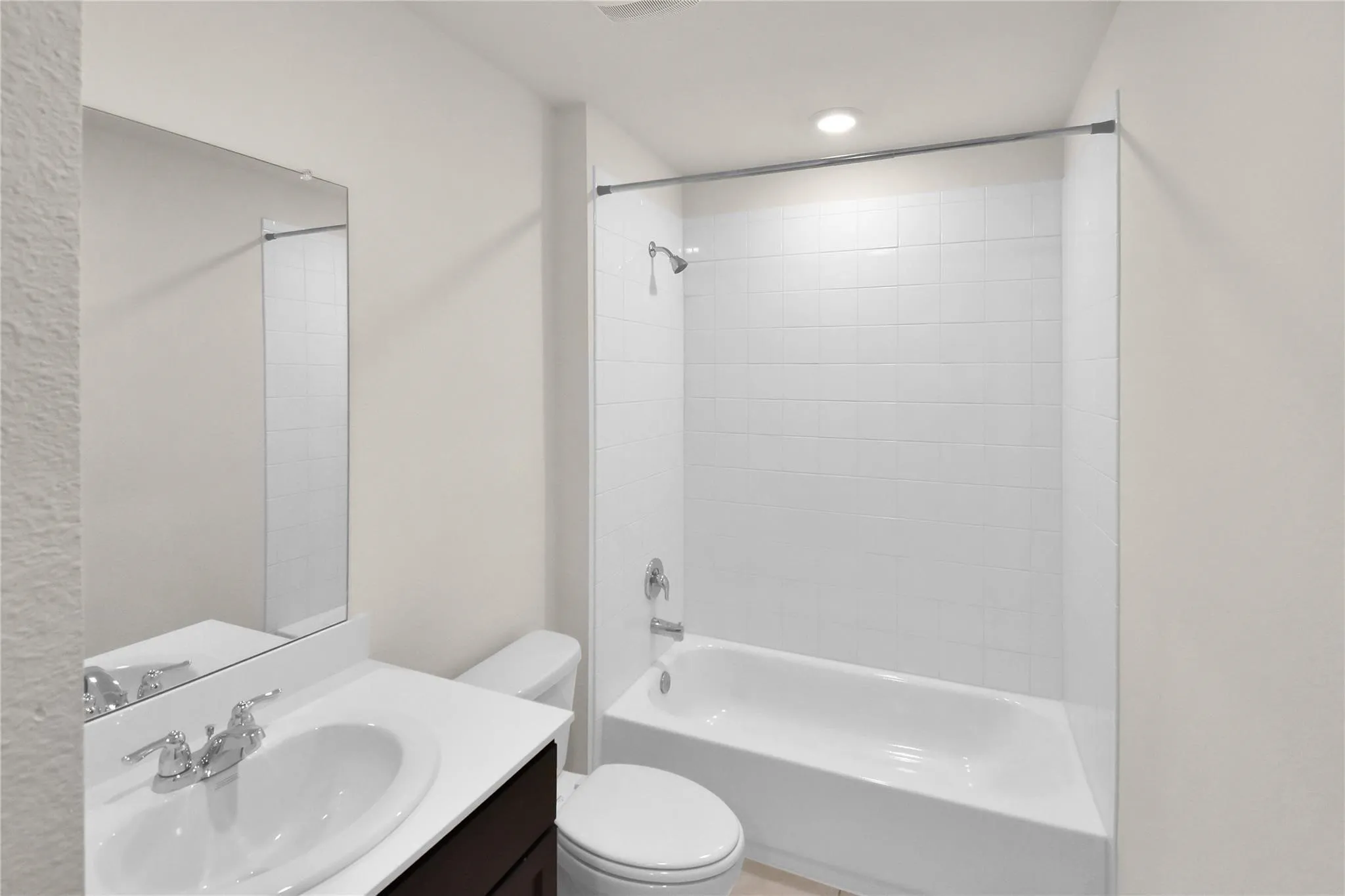 White subway tile shower surround with a tub, recessed lighting, a vanity with a white countertop, and a chrome faucet
