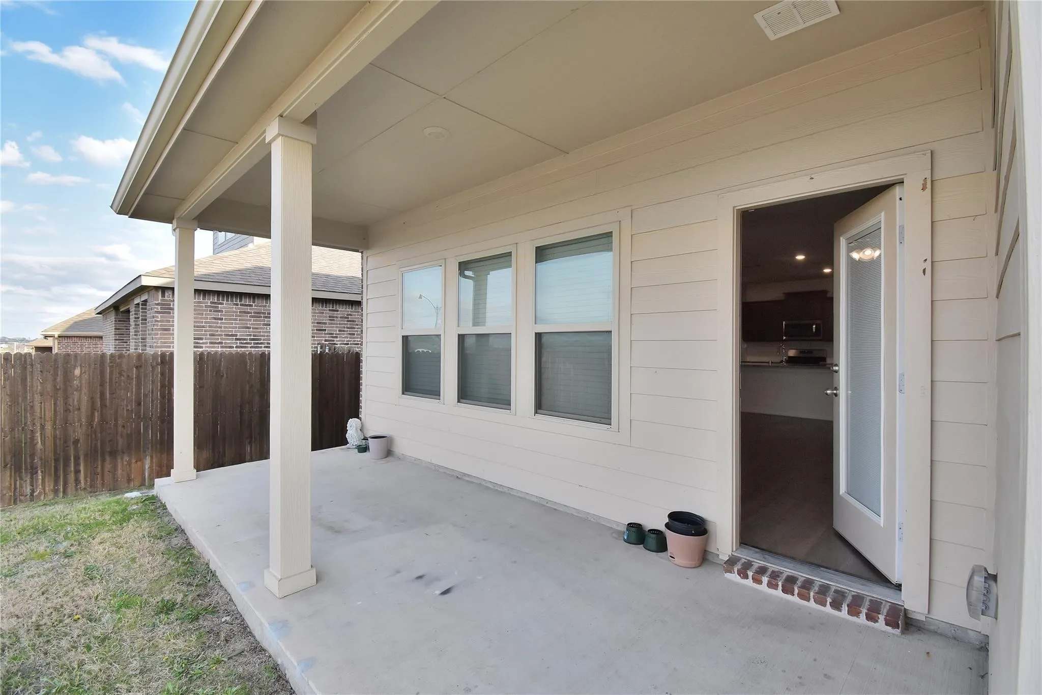 Covered patio with concrete flooring, supported by two columns, featuring exterior siding and a privacy fence