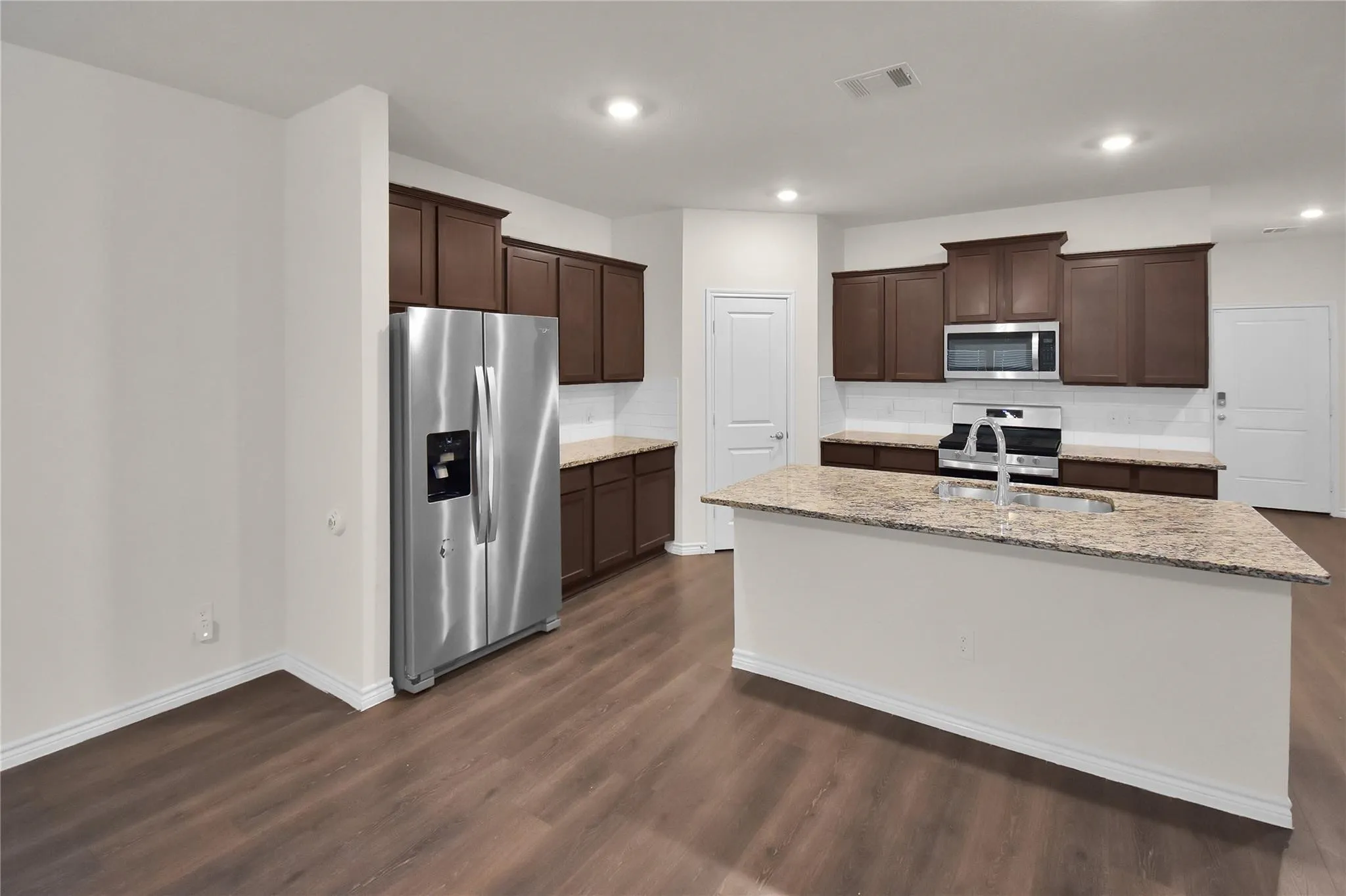 Kitchen featuring an island with a sink, stainless steel appliances, dark wood-finish cabinetry, and wood-finish flooring