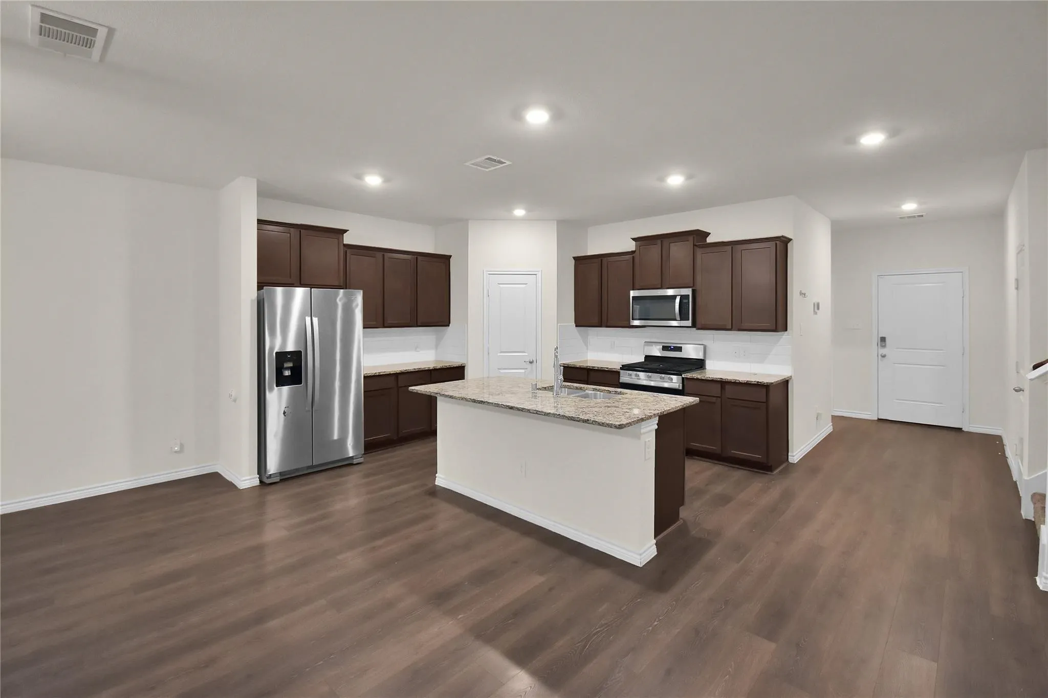 Open-concept kitchen featuring dark wood cabinetry, light countertops, a central island, stainless steel appliances, and wood-finish flooring