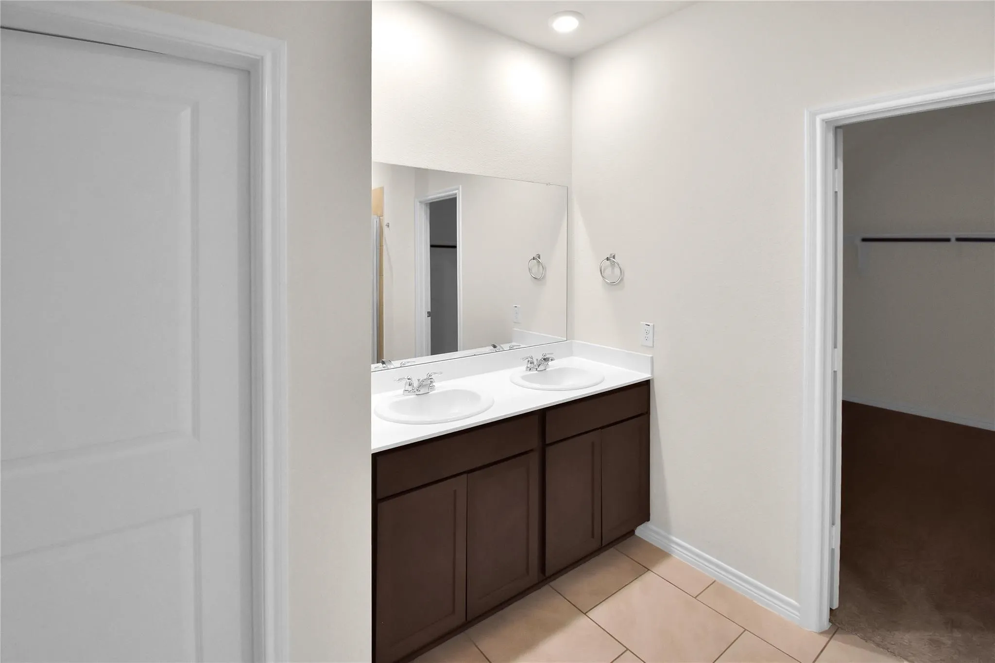 Dual vanity with an expansive mirror, recessed lighting, tile flooring, and dark wood-finish cabinetry