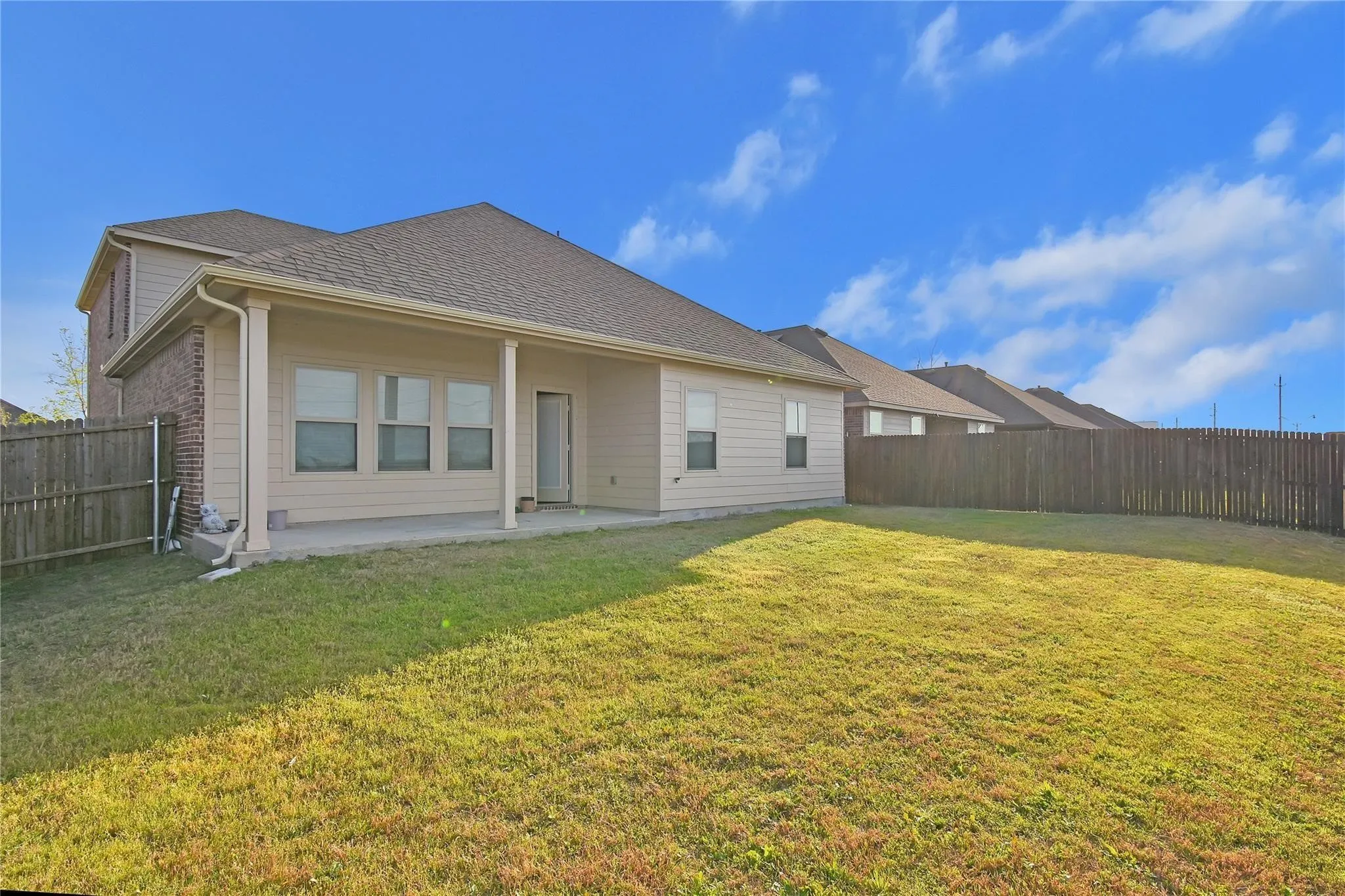 Expansive backyard featuring a covered patio, brick and siding exterior, and wood fencing