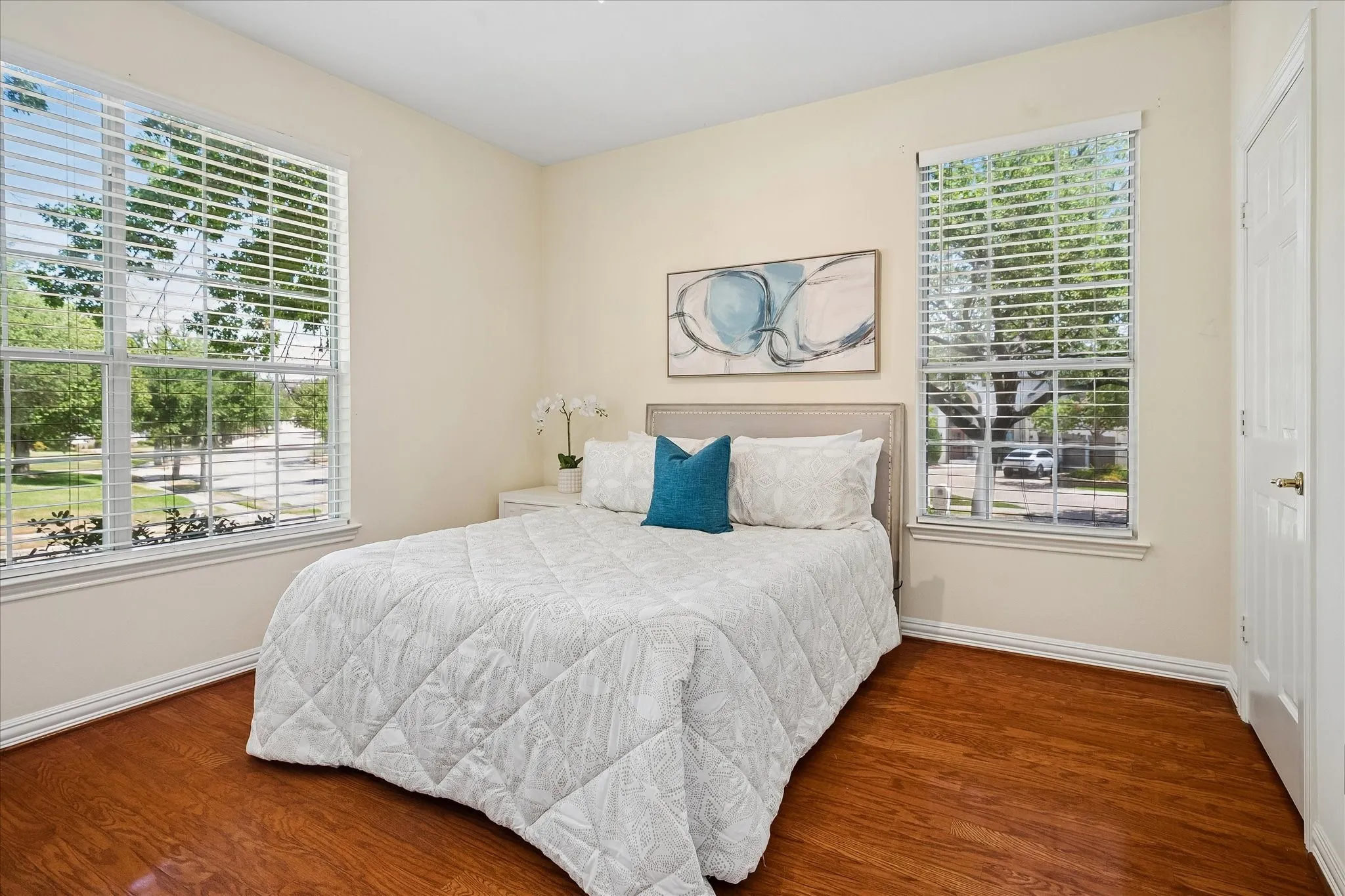 Hardwood flooring, multiple windows with blinds, light-toned wall paint, and white trim throughout