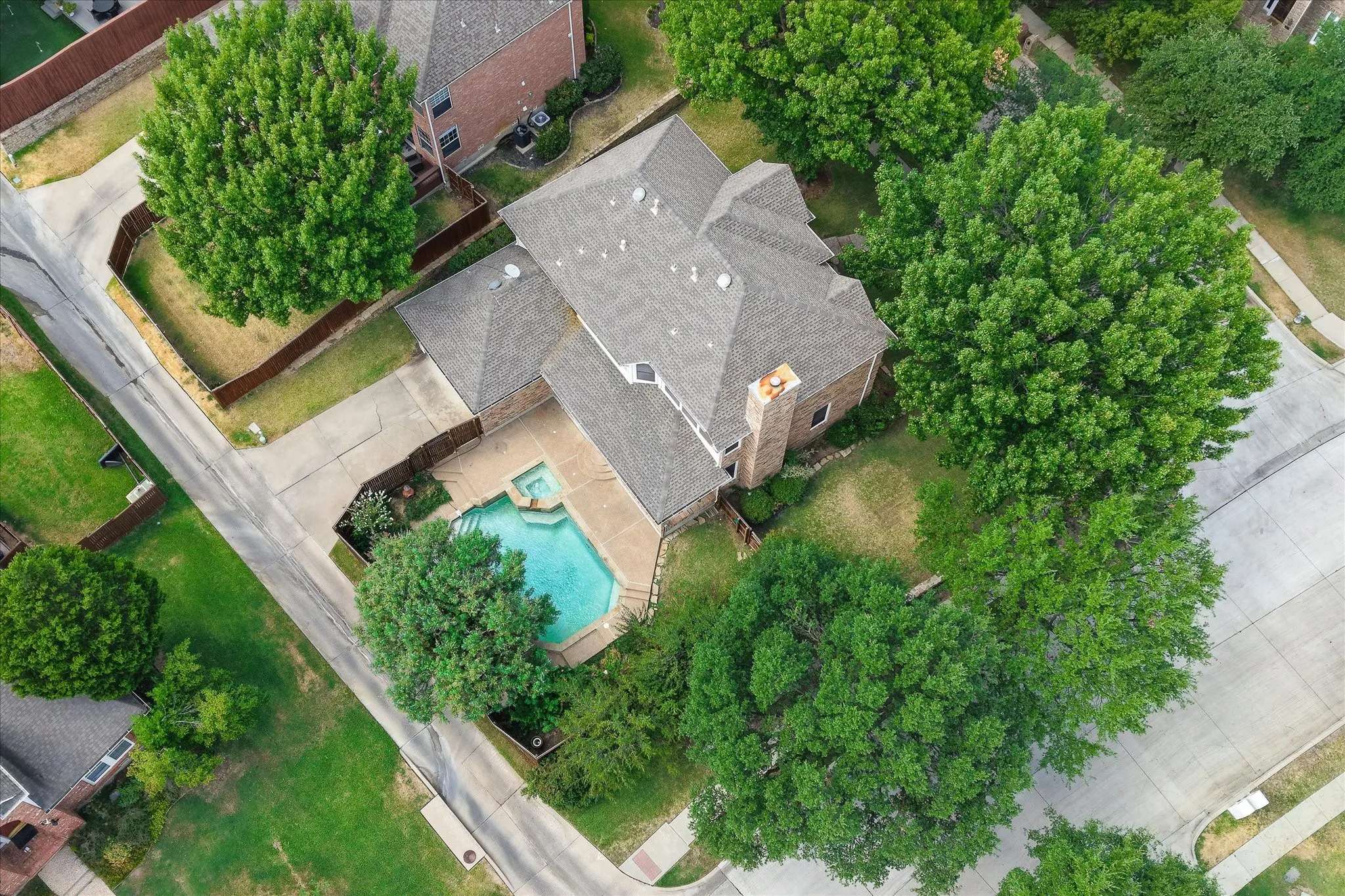 Expansive property featuring a private swimming pool with integrated spa, mature trees, a brick chimney, and concrete driveways