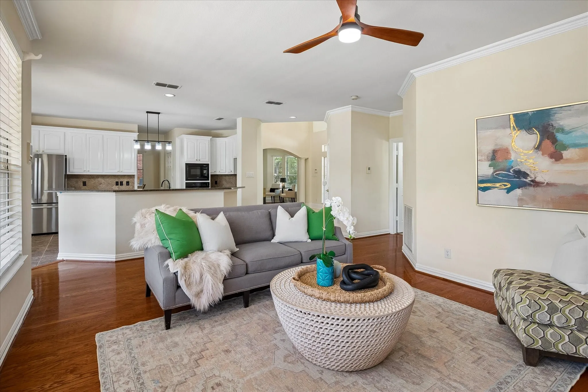Wood-finish flooring, ceiling fan with integrated lighting, recessed lighting, and kitchen with white cabinetry and stainless steel appliances