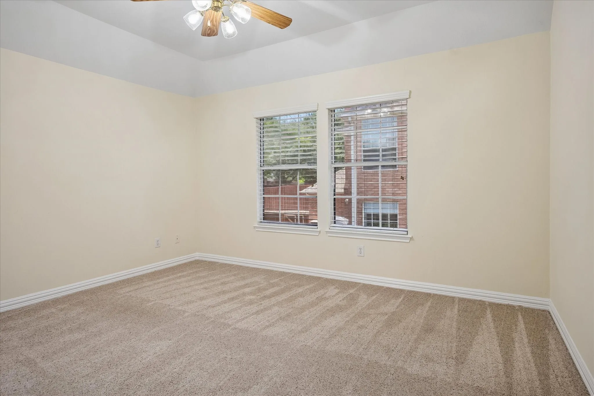 Tray ceiling, ceiling fan with light fixture, two windows with blinds, neutral tone walls, and carpet flooring