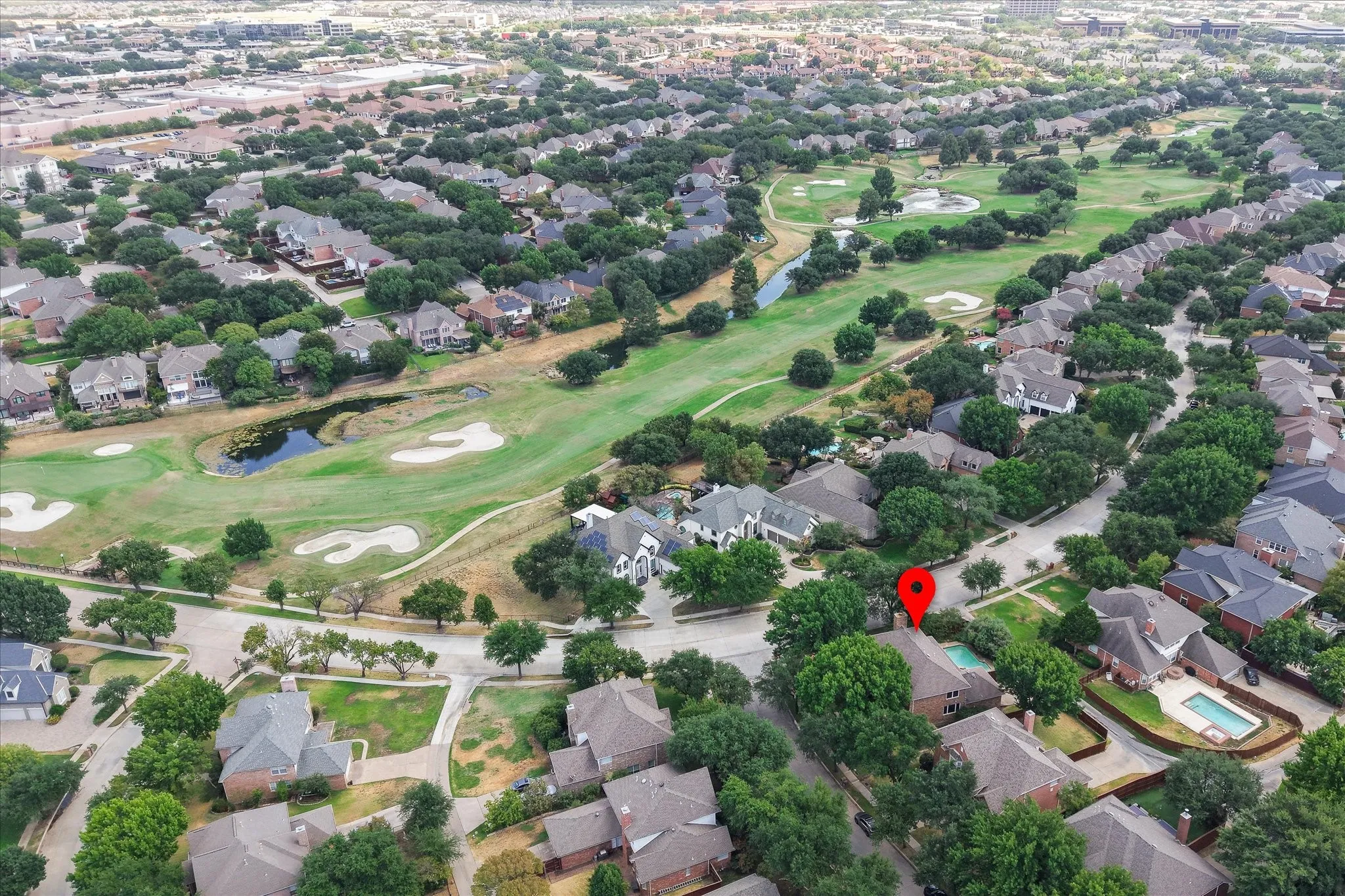 Aerial perspective showcasing a residential area with mature trees, green spaces, and a golf course with water features