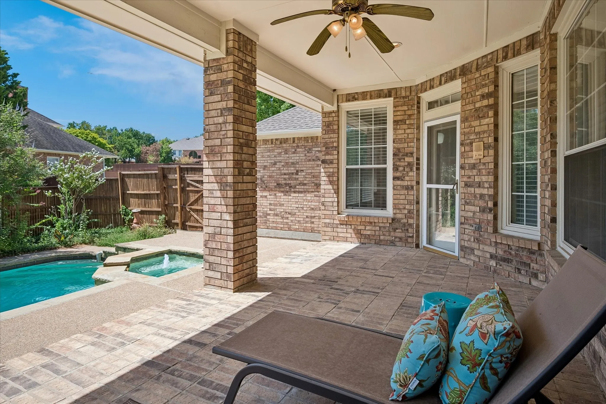 Covered patio with brick columns, paver flooring, ceiling fan, and access to a swimming pool with an integrated spa