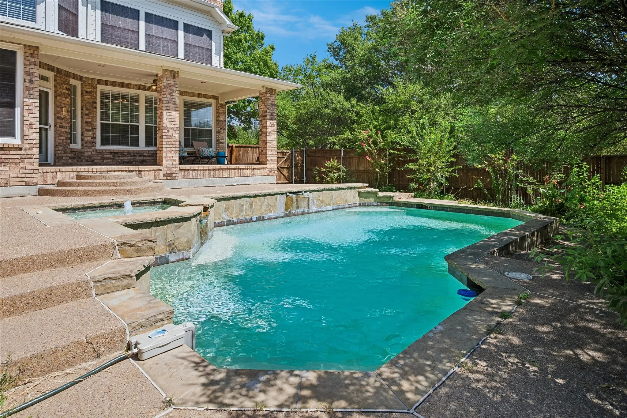 Outdoor swimming pool with integrated spa and waterfall feature, complemented by a covered patio with brick columns