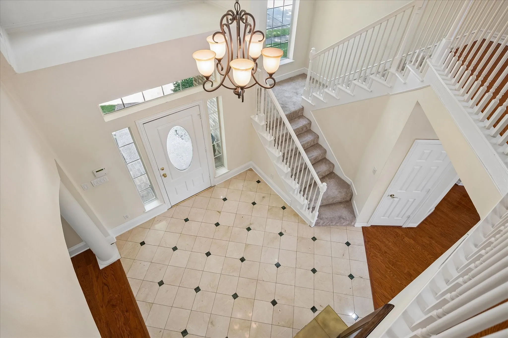 Two-story foyer featuring a decorative chandelier, tile flooring with dark accent tiles, and a white front entry door with an oval glass insert