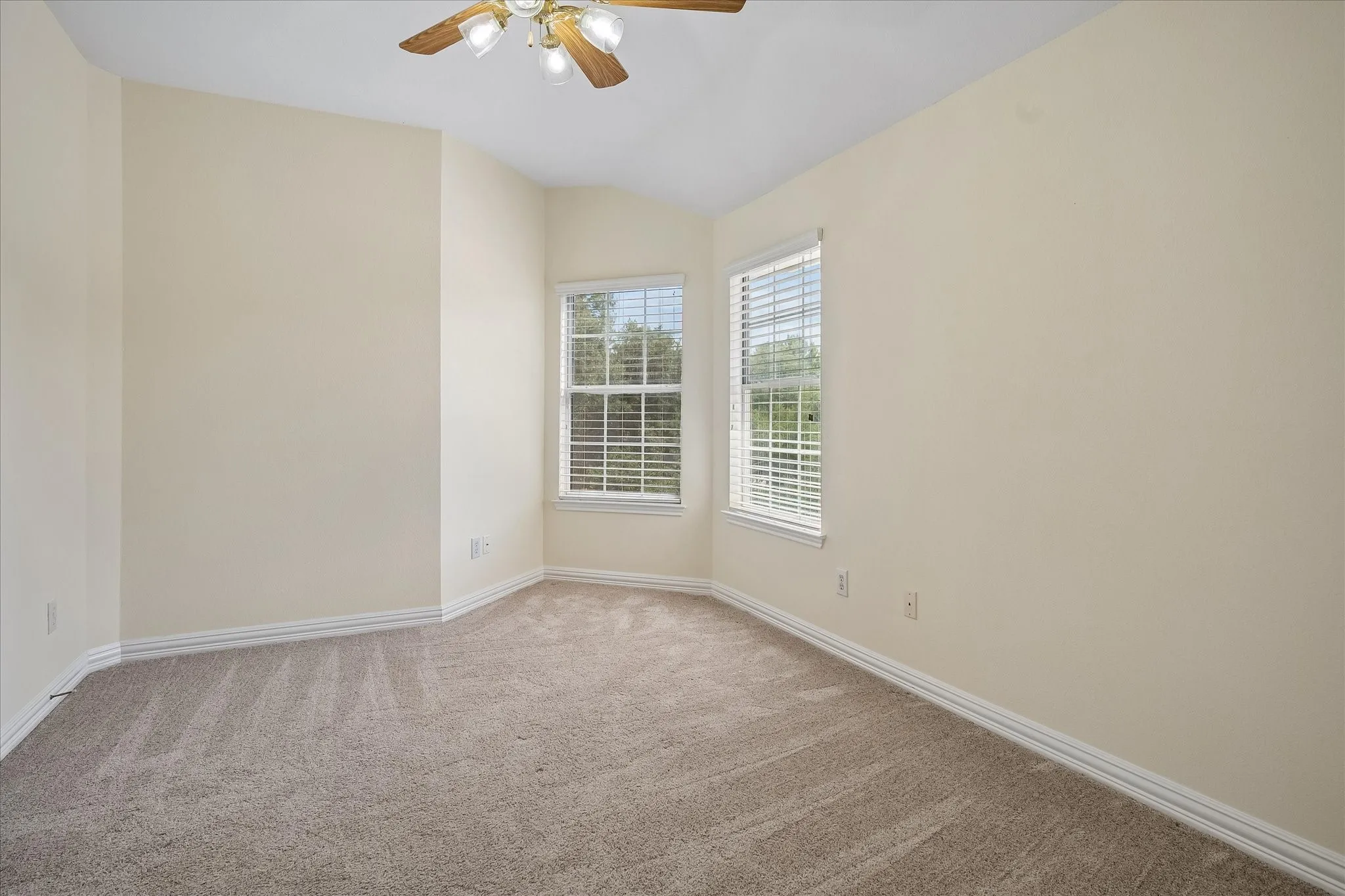 Carpeted interior space with a ceiling fan light fixture, two windows with blinds, and neutral painted walls