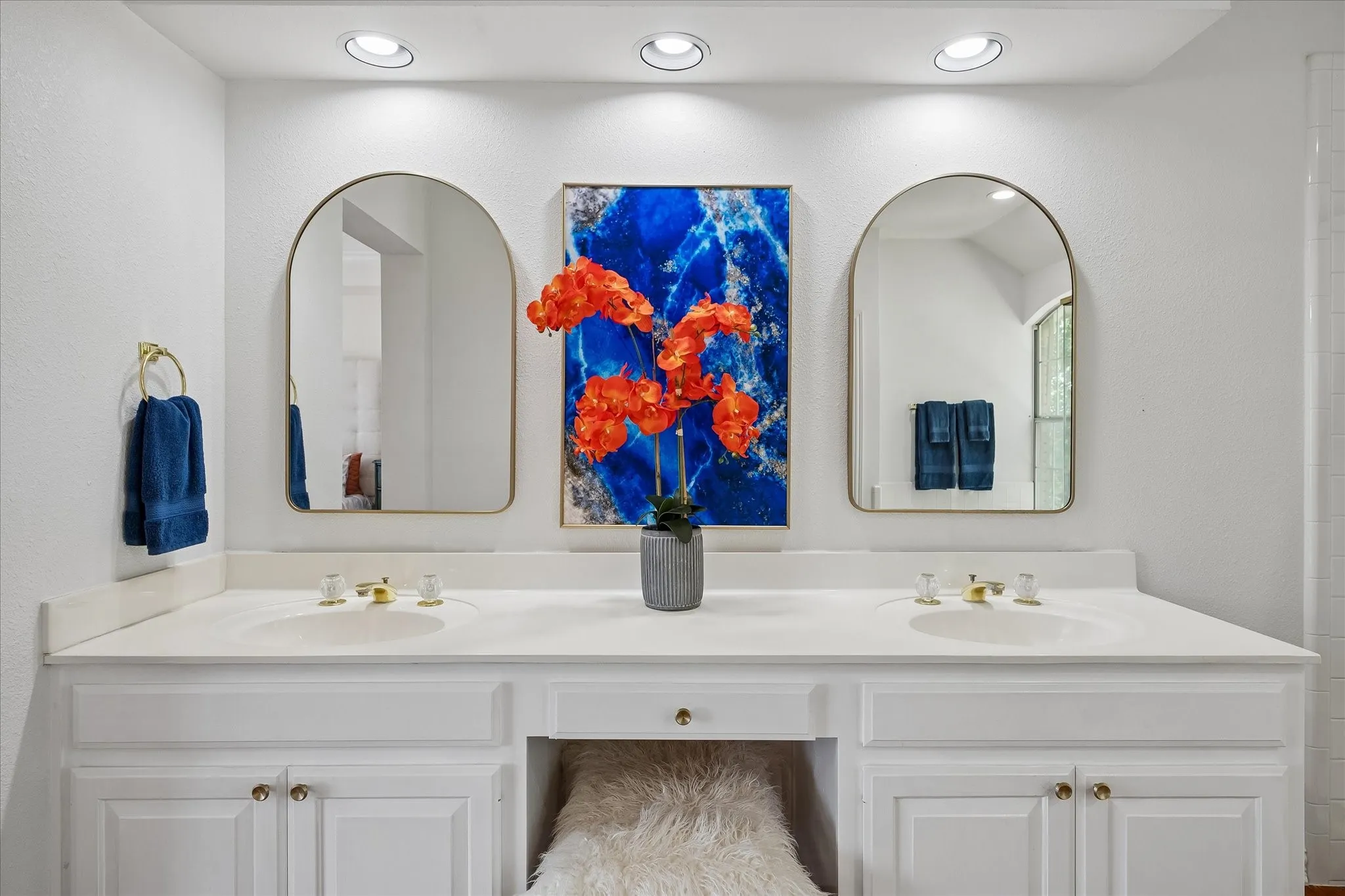 Dual arched mirrors above a vanity with two integrated sinks, gold-finish faucets, and recessed lighting
