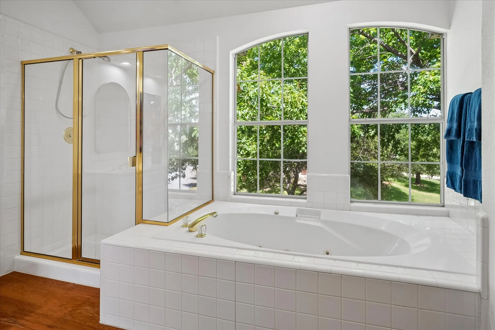 Soaking tub with brass-finish fixtures, tile surround, and two arched windows