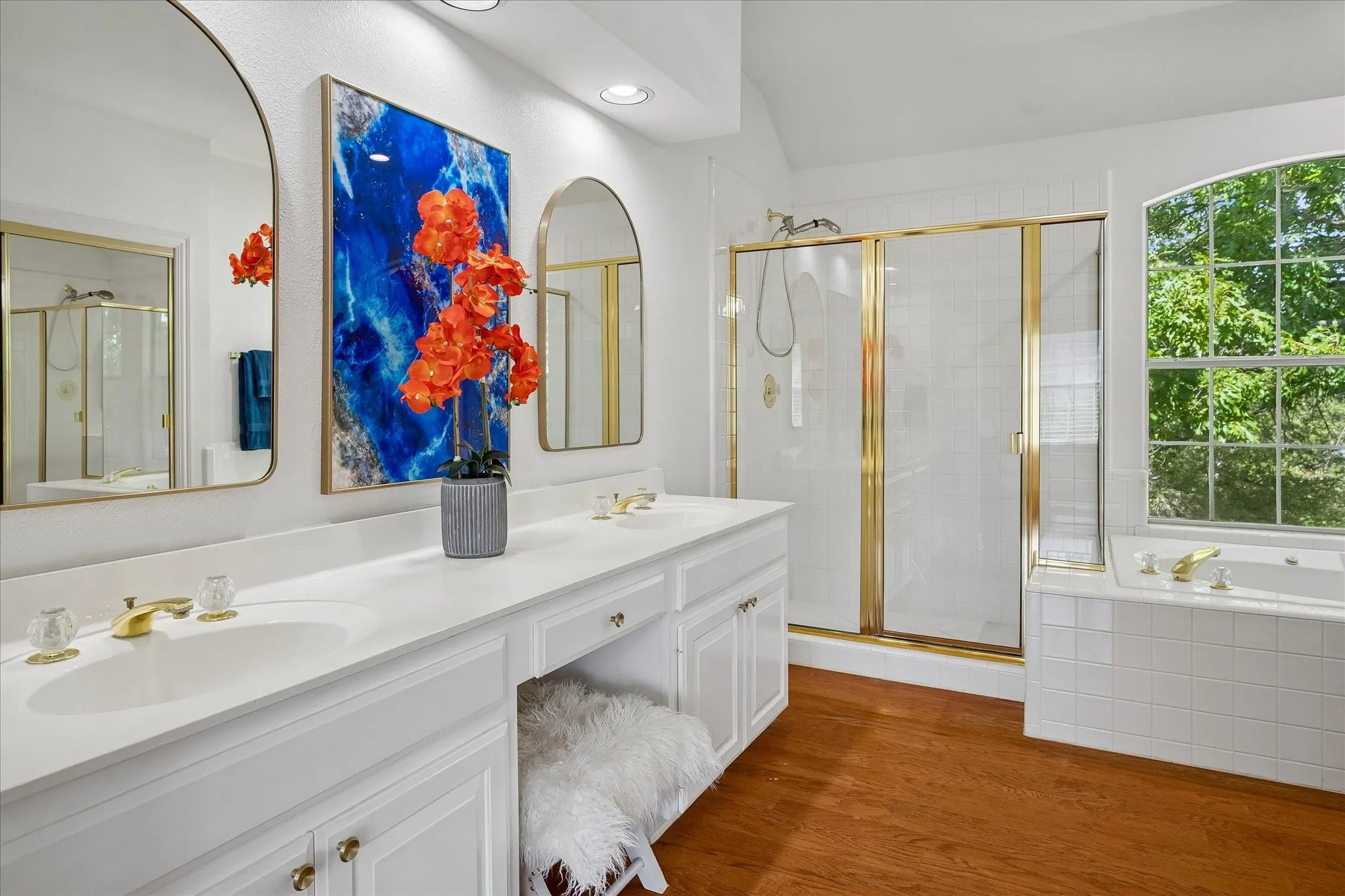 Dual vanity with integrated sinks, built-in makeup area, wood-finish flooring, gold-finish shower enclosure, and a built-in bathtub