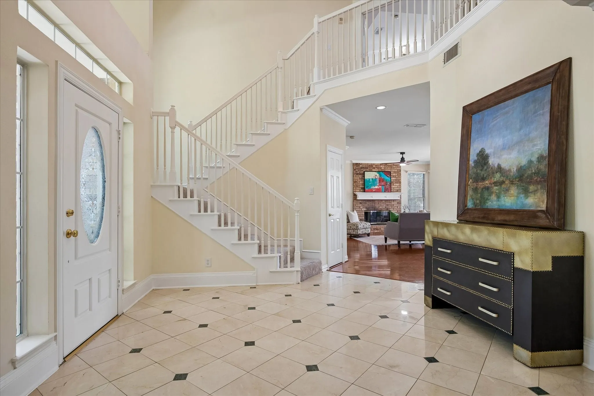 Two-story foyer featuring tile flooring with dark accent squares, a white staircase with balusters, and a solid wood front door with an oval glass insert