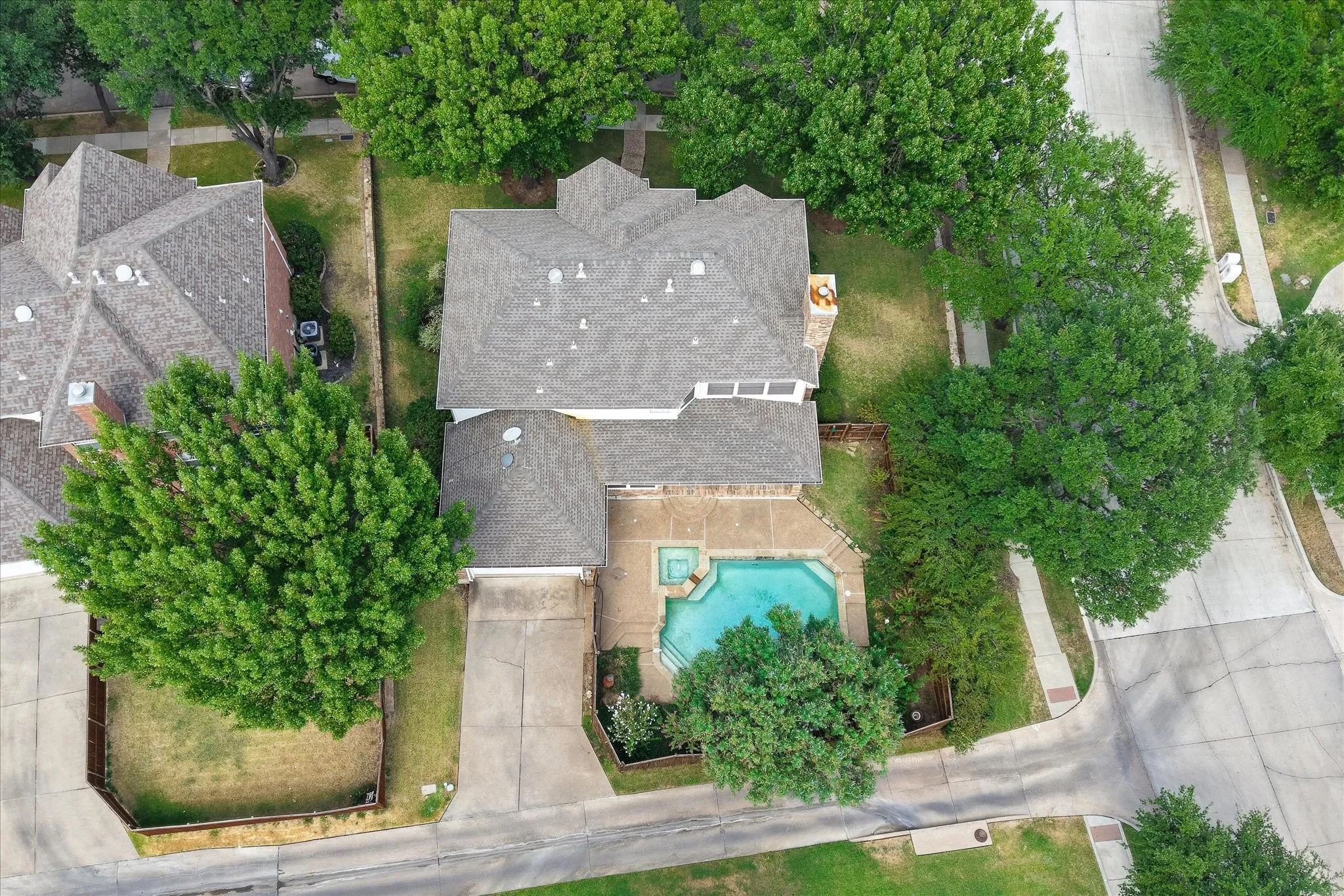 Residential property featuring a shingled roof, a paved driveway, and an in-ground pool with surrounding hardscaping