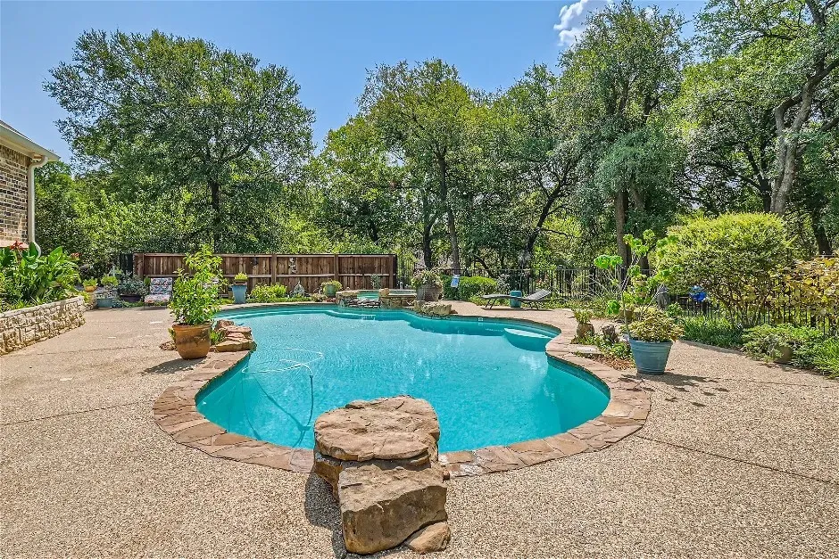 Freeform swimming pool with stone coping, surrounded by an exposed aggregate patio