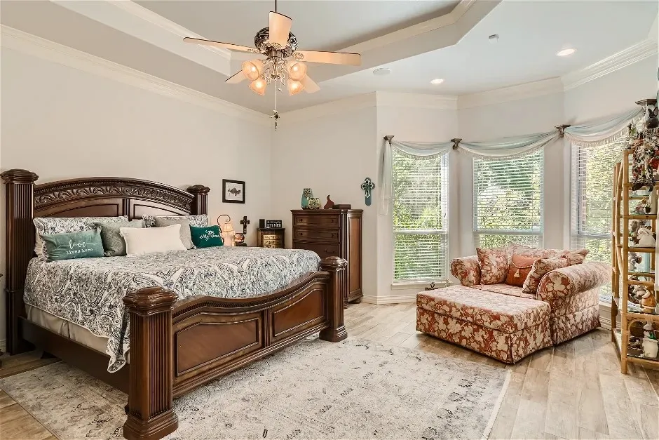 Tray ceiling with crown molding, wood-finish flooring, recessed lighting, and a bay window