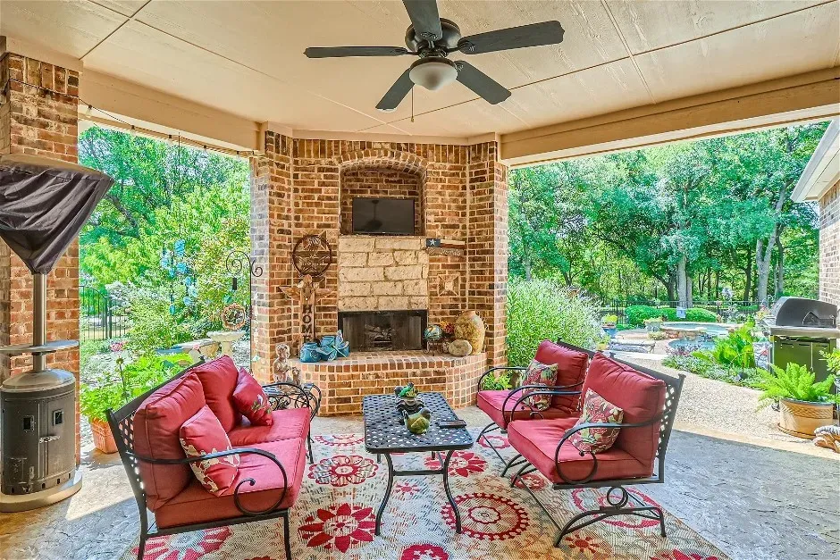 Covered patio featuring a brick fireplace with stone accents, a built-in television niche, a ceiling fan, and concrete flooring