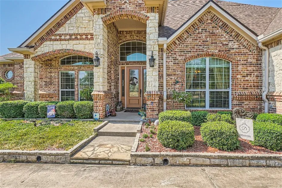 Brick and stone exterior featuring arched windows, a covered entry with a glass-paneled door, and a concrete and flagstone walkway