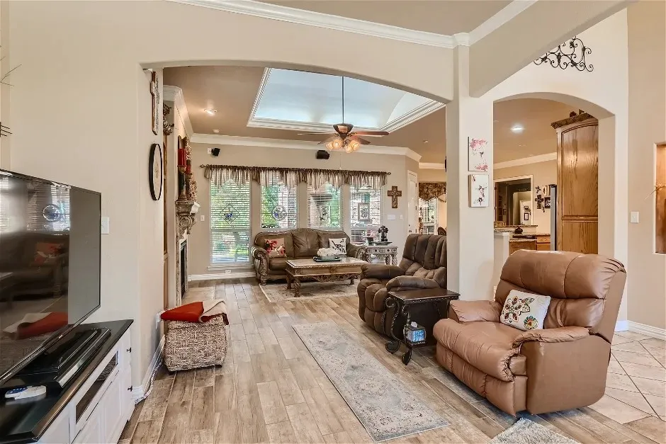 Wood-finish flooring throughout, tray ceiling with recessed lighting, crown molding, and an arched doorway