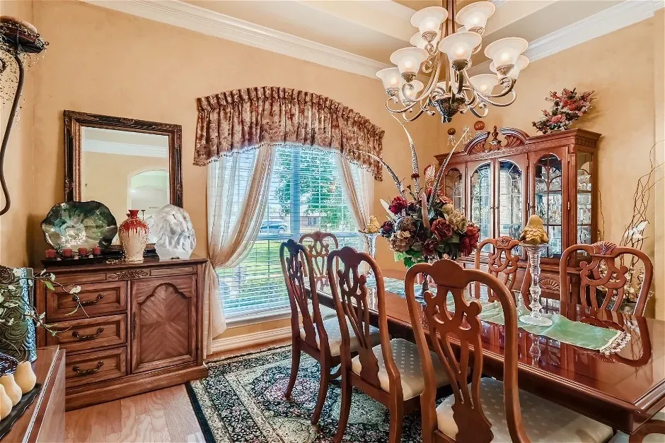 Tray ceiling with crown molding, chandelier with frosted glass shades, wood-finish flooring, bay window with decorative valance, built-in display cabinet
