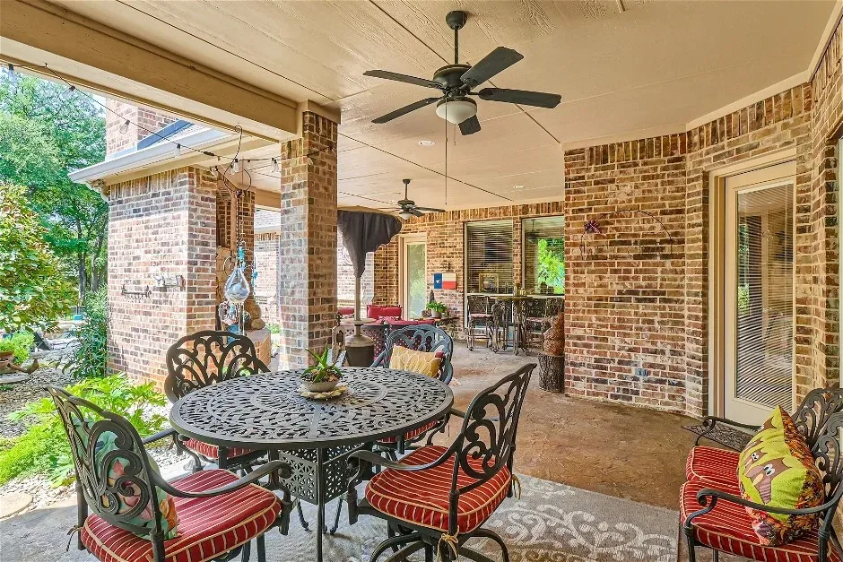 Covered patio featuring brick masonry, dual ceiling fans, and an exterior door with privacy blinds