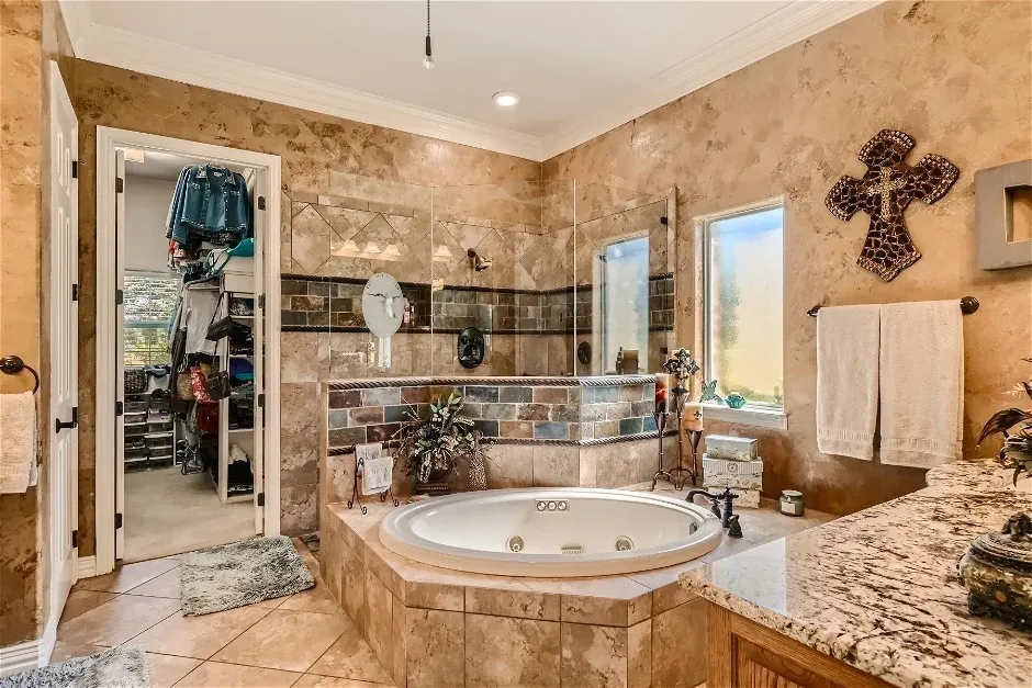 Soaking tub with tile surround, walk-in shower with glass enclosure, dual windows, granite countertop vanity, and an adjacent walk-in closet