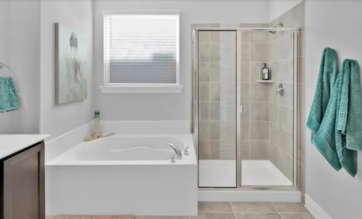 White soaking tub, glass-enclosed shower with tiled walls, and light-toned floor tile