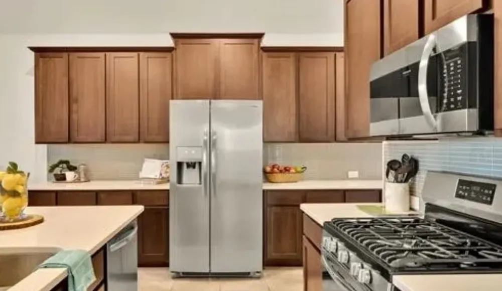 Stainless steel appliances, wood-finish cabinetry, light-toned countertops, tile backsplash, and a gas range