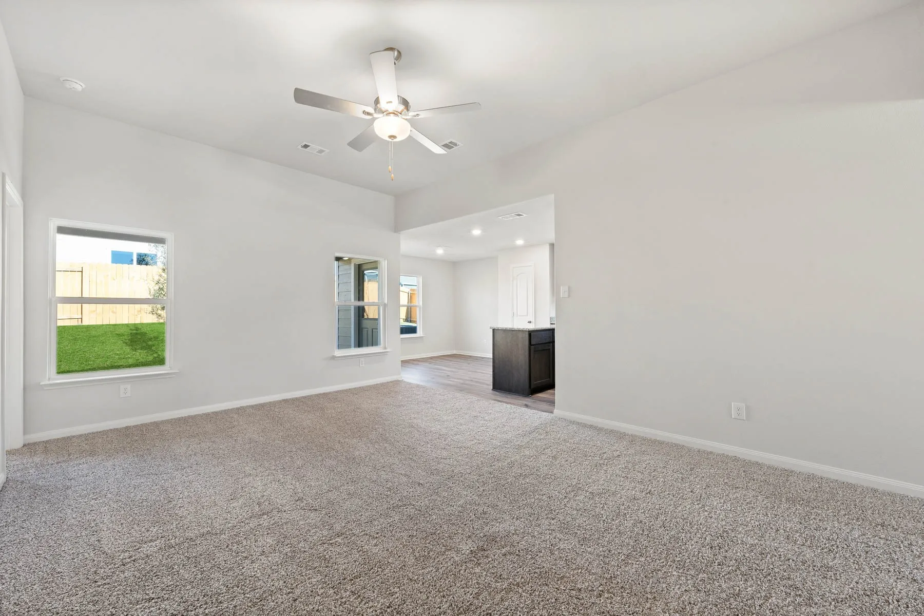 Unfurnished living room featuring ceiling fan, light colored carpet, and a healthy amount of sunlight