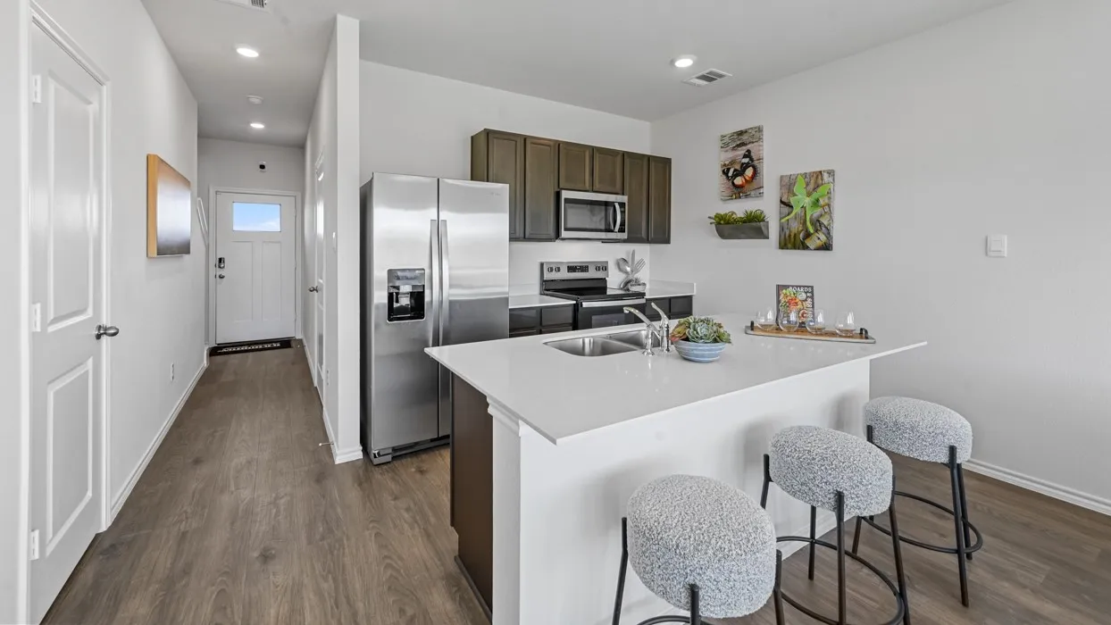 Kitchen featuring dark wood-finish cabinetry, stainless steel appliances, a white countertop island with an undermount sink, and wood-finish flooring