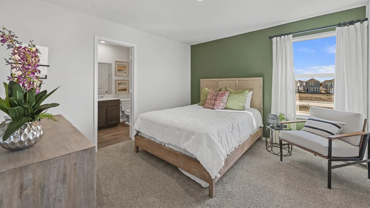Plush carpeting, a large window, and an en-suite bathroom with a dark wood-finish vanity and wood-finish flooring