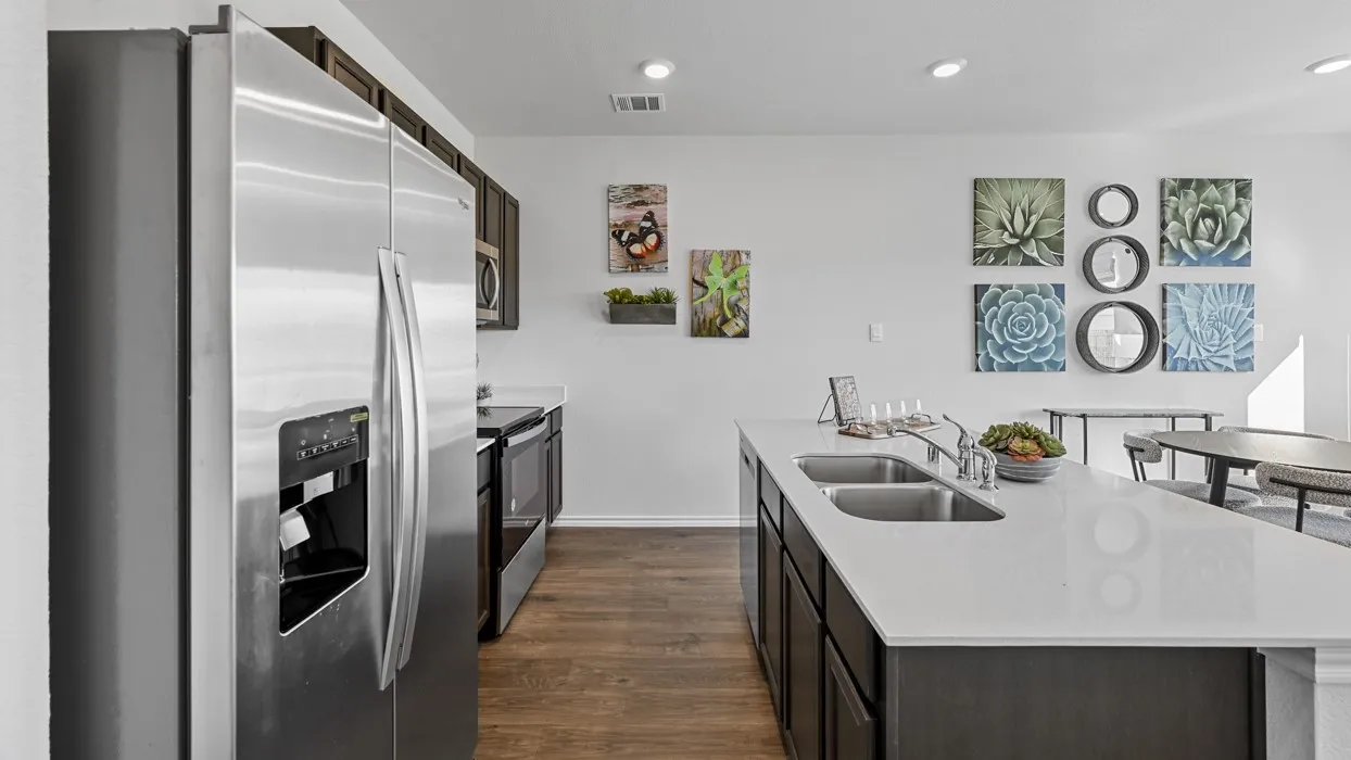 Kitchen featuring stainless steel appliances, dark wood cabinetry, a center island with a double sink, light-toned countertops, and wood-finish flooring