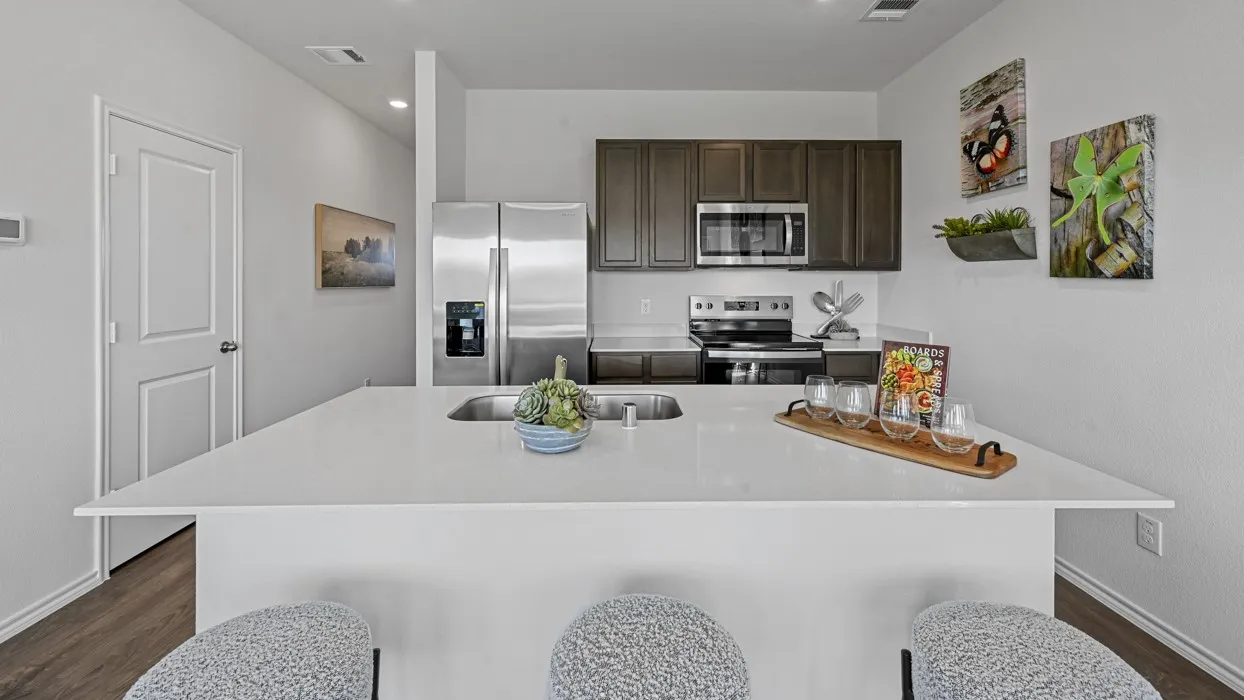 Spacious kitchen featuring a large island with a built-in sink, stainless steel appliances, dark wood-finish cabinetry, and light countertops