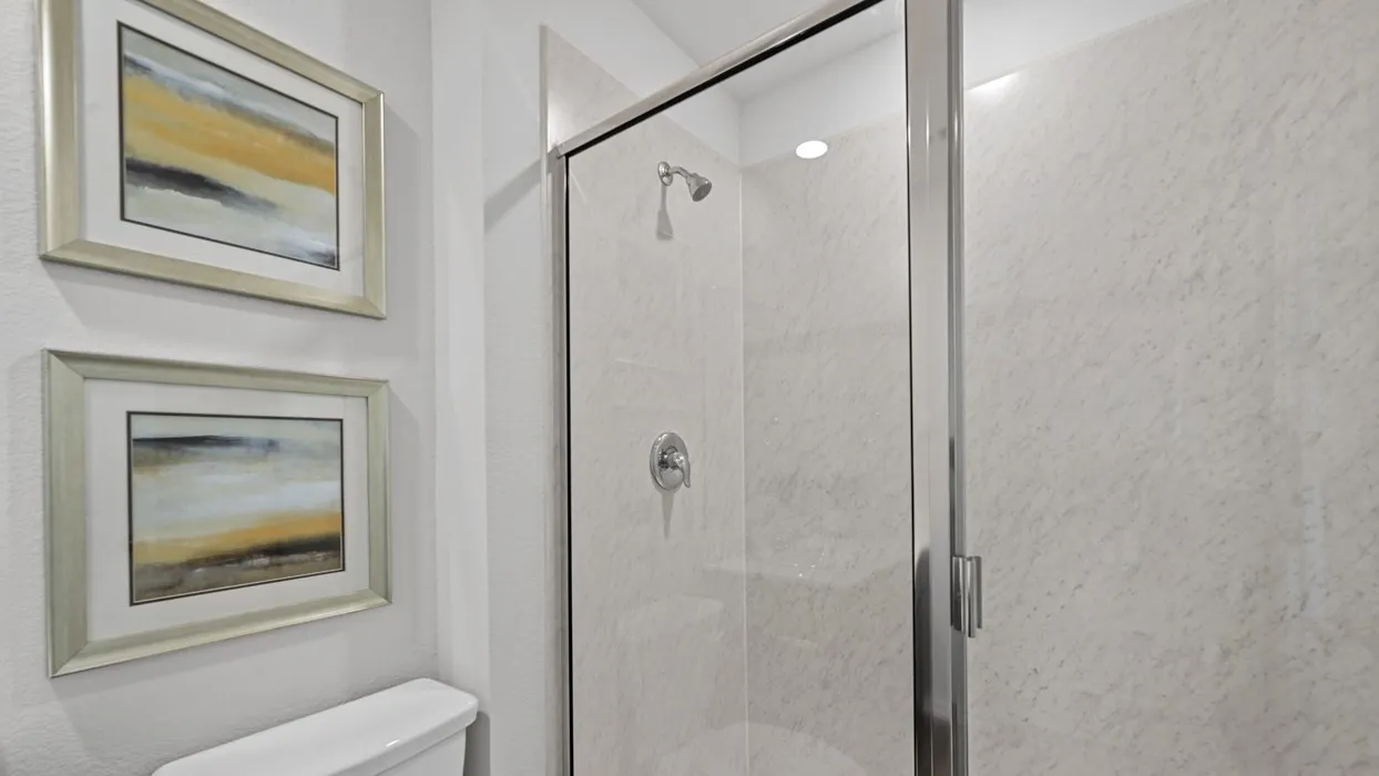 Glass-enclosed shower with a chrome shower head and handle, complemented by light-toned wall paneling
