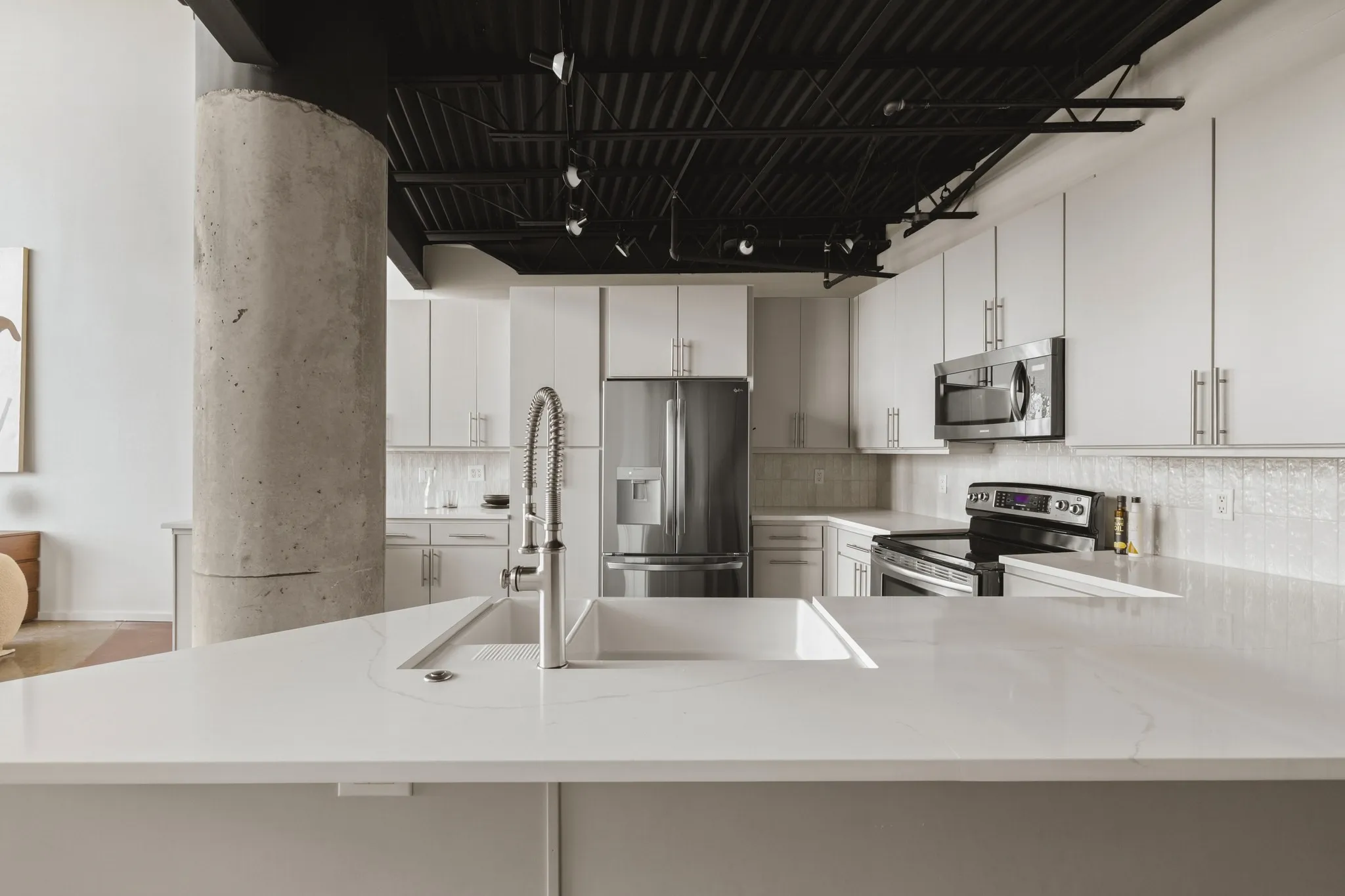 Modern kitchen featuring white cabinetry, stainless steel appliances, a white basin sink with a chrome faucet, and exposed concrete column