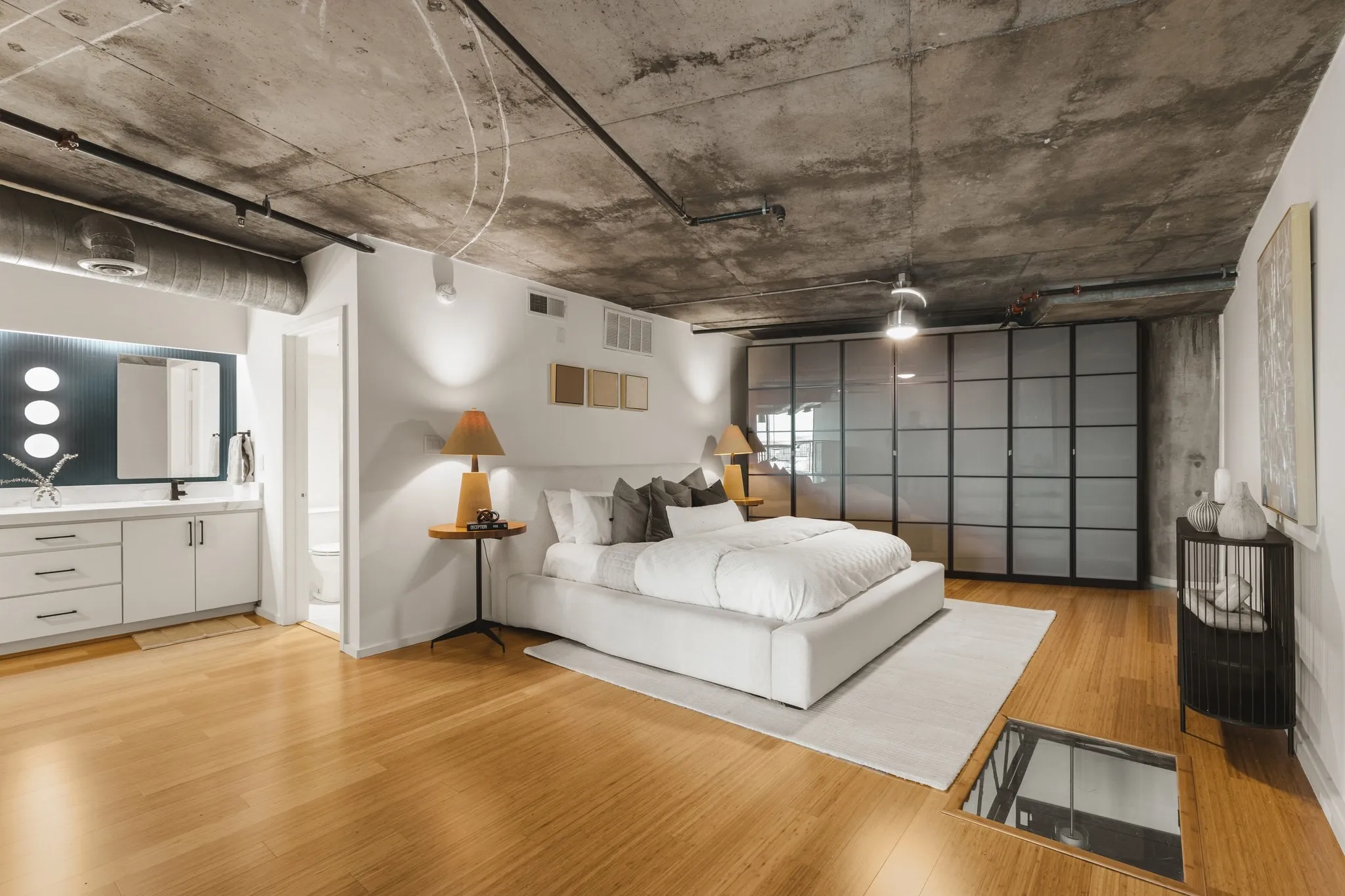 Concrete ceiling with exposed ductwork, wood-finish flooring, built-in wardrobe with frosted glass panels, vanity with white cabinetry and undermount sink, and recessed lighting