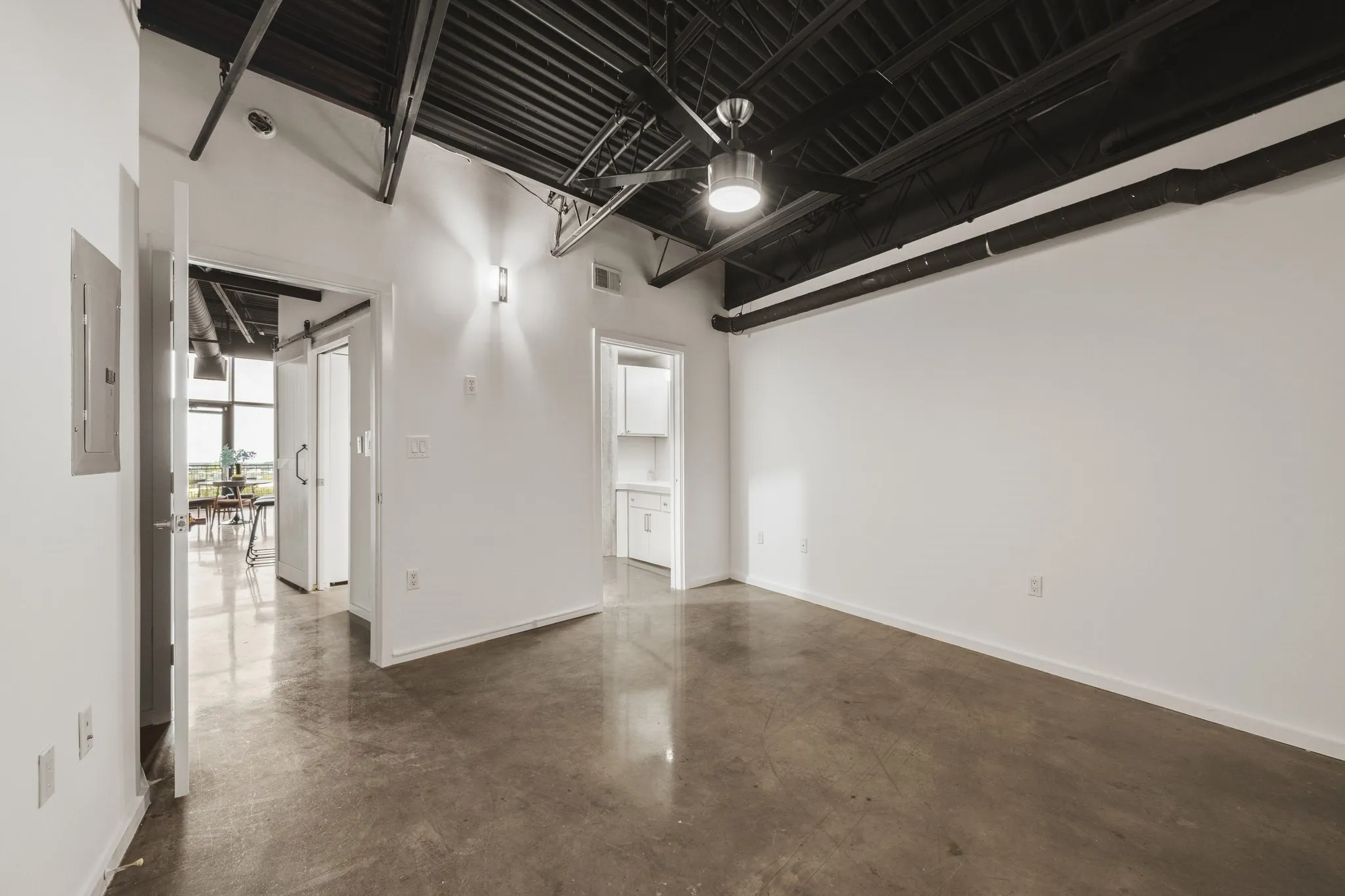 Exposed ceiling beams, industrial-style ceiling fan, polished concrete flooring, white walls, and contemporary wall sconce