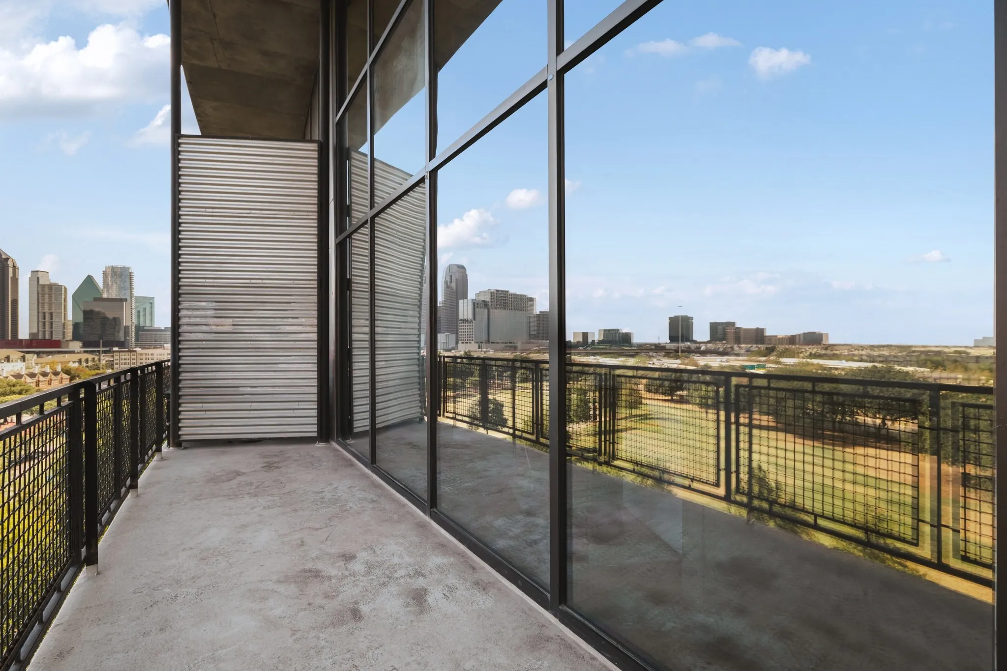 Expansive balcony with a concrete floor, black mesh railing, and floor-to-ceiling windows