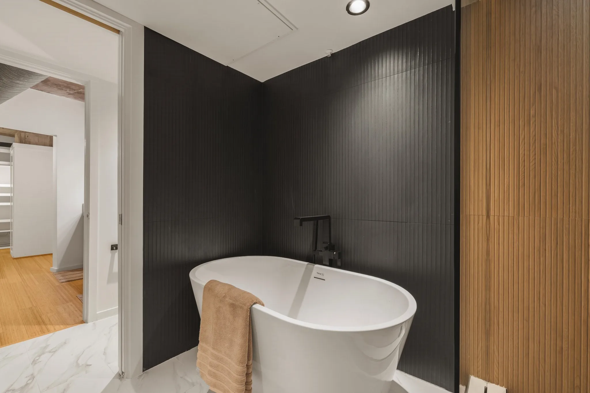 Freestanding soaking tub with matte black fixtures, set against a dark fluted accent wall