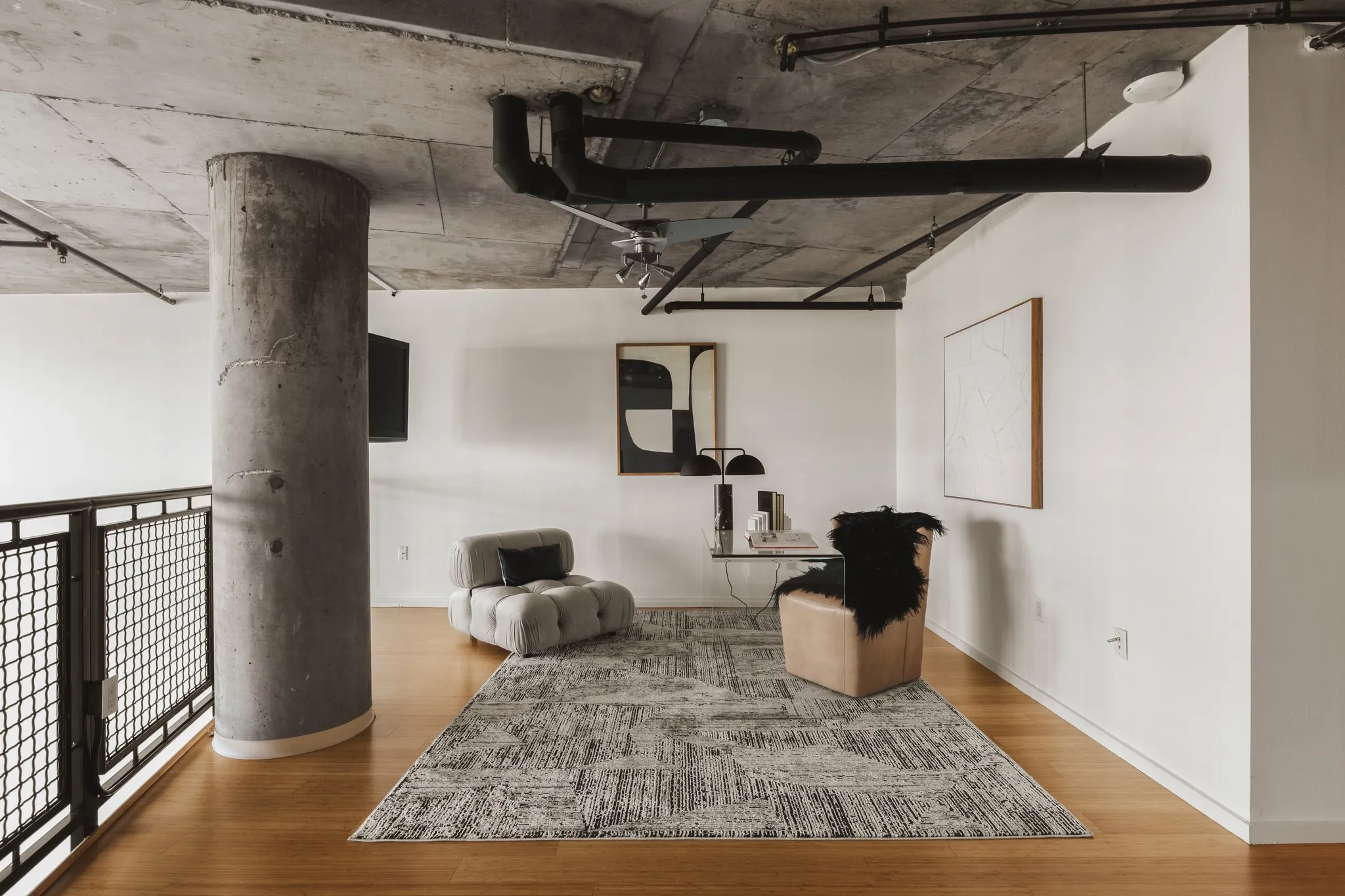 Exposed concrete ceiling, industrial-style black piping, concrete structural column, light wood-finish flooring, and white painted walls