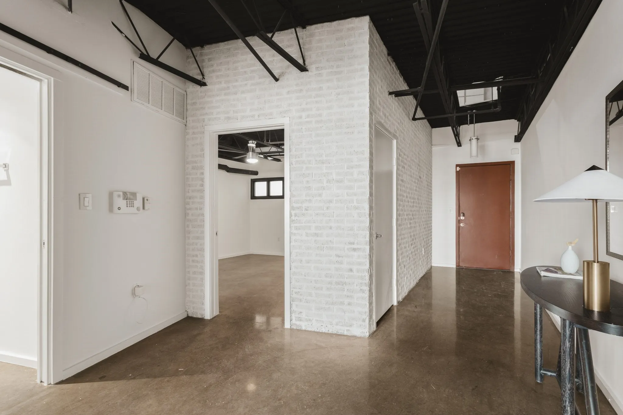 Polished concrete flooring, white painted brick accent wall, exposed black ceiling joists, recessed ceiling lighting, and a solid core entry door